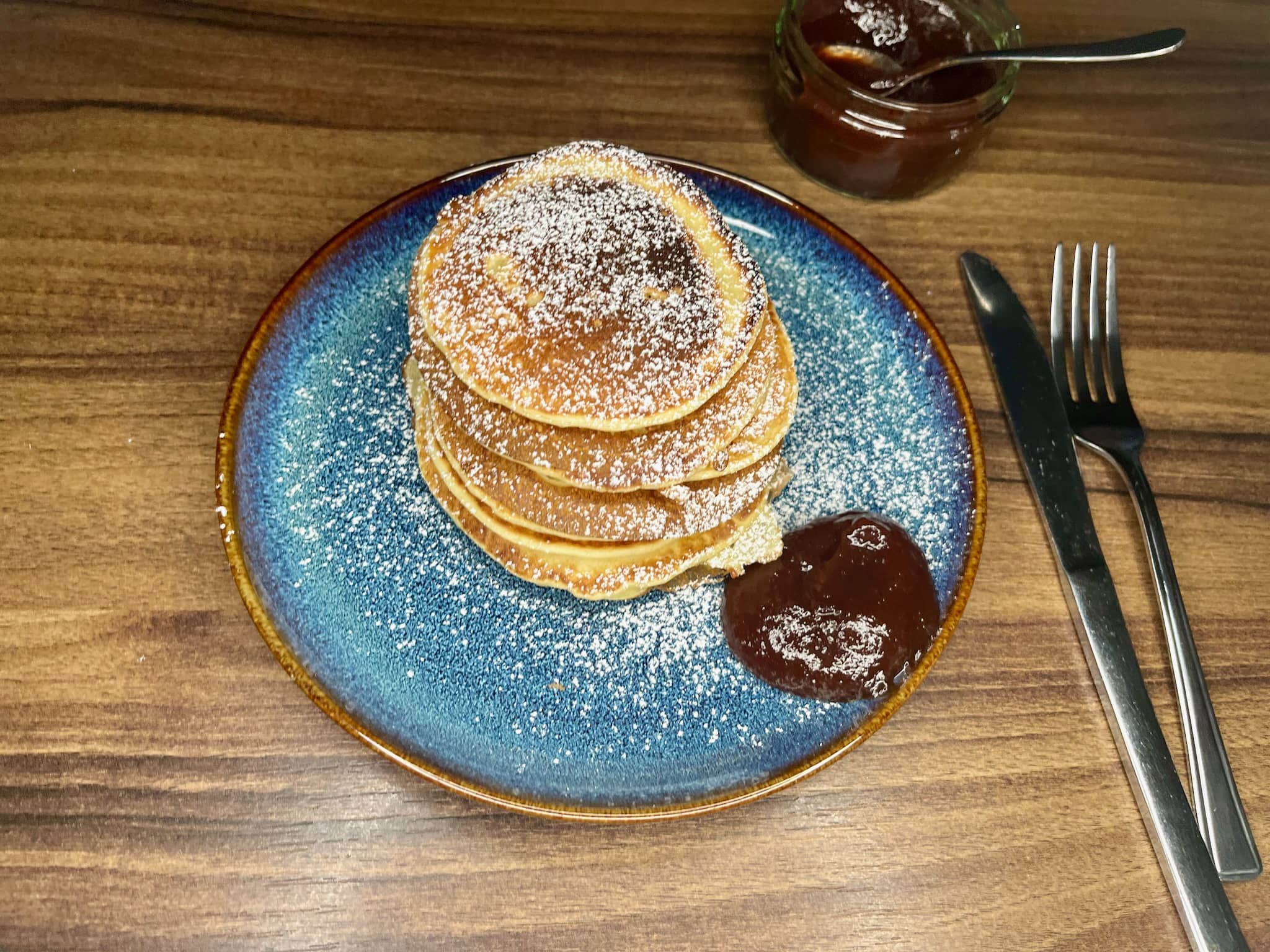 American pancakes in stack on a plate dusted with icing sugar and served with jam