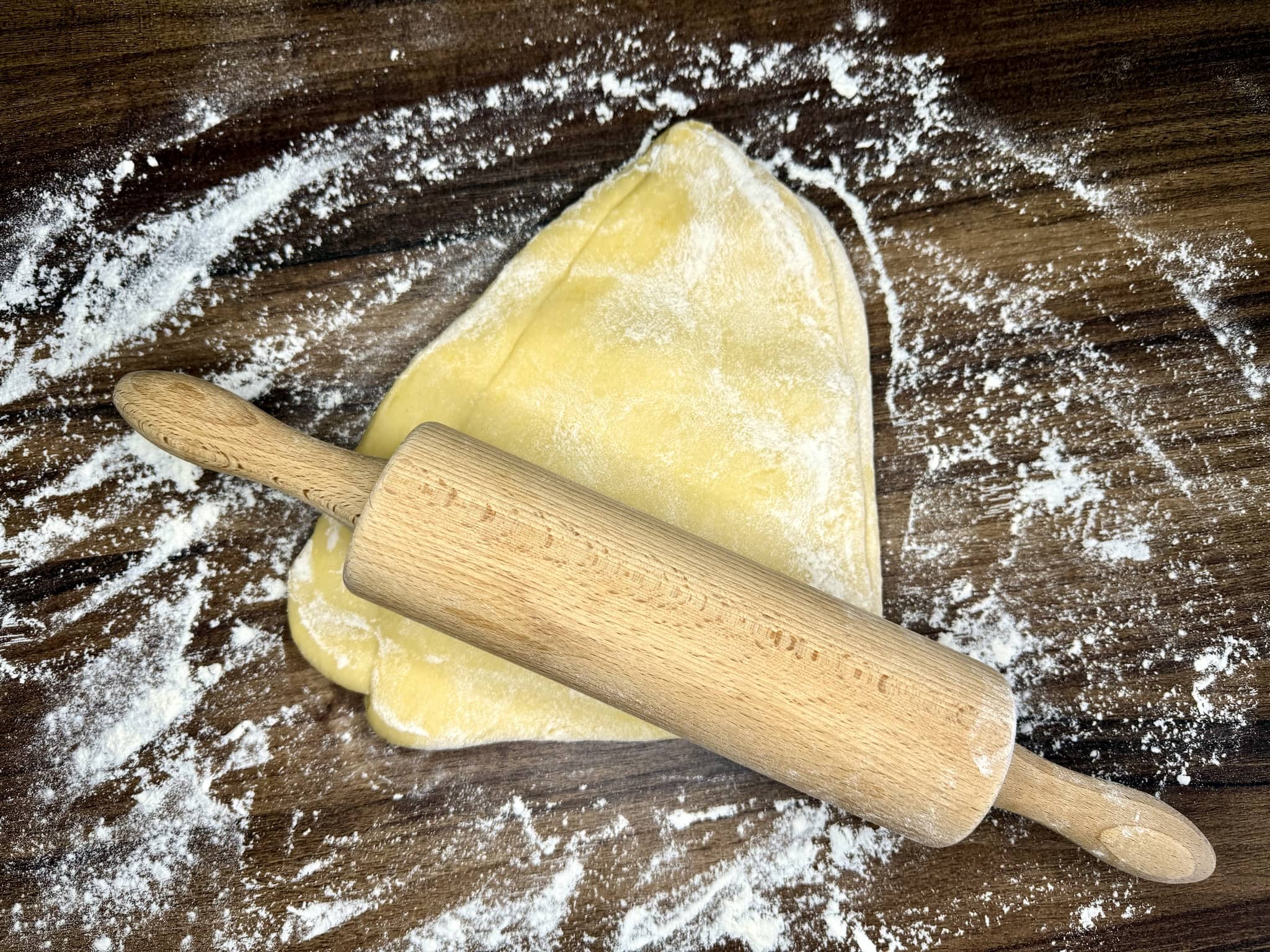 Rolling of a dough ball in progress with rolling pin resting on top of the dough