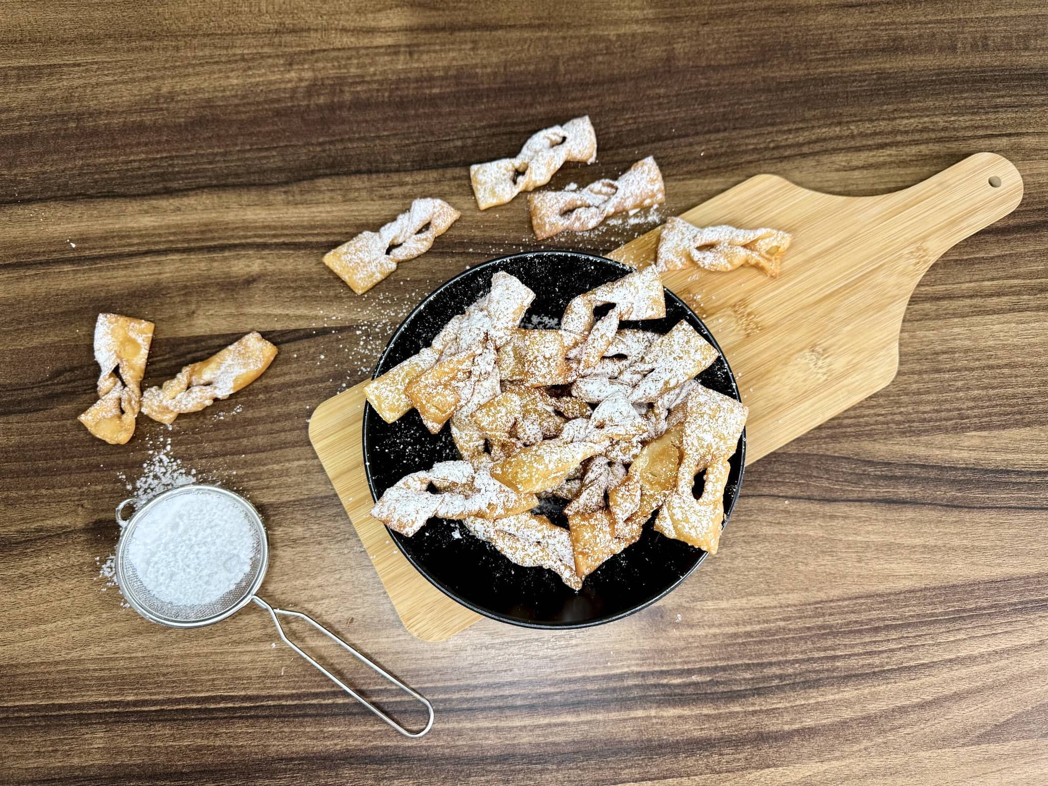 Fried angel wings on a plate, on top of a chopping board, dusted intensively with icing sugar