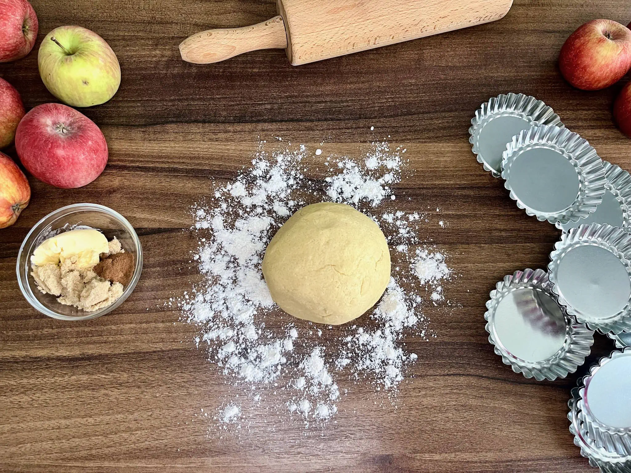 A ball of dough sits on a dusted tabletop, surrounded by other ingredients