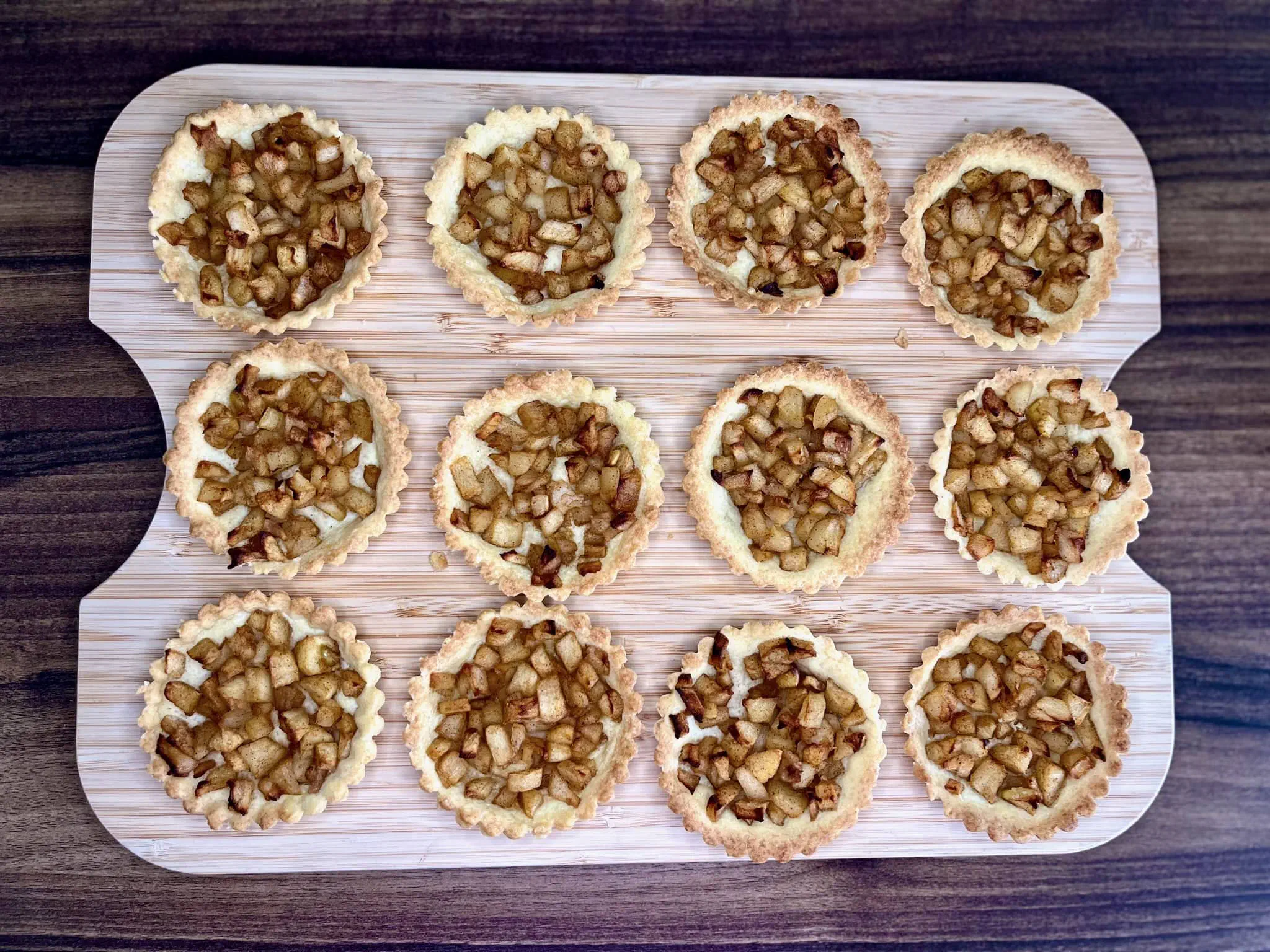 Mini apple tarts, baked and removed from tins, resting on a chopping board