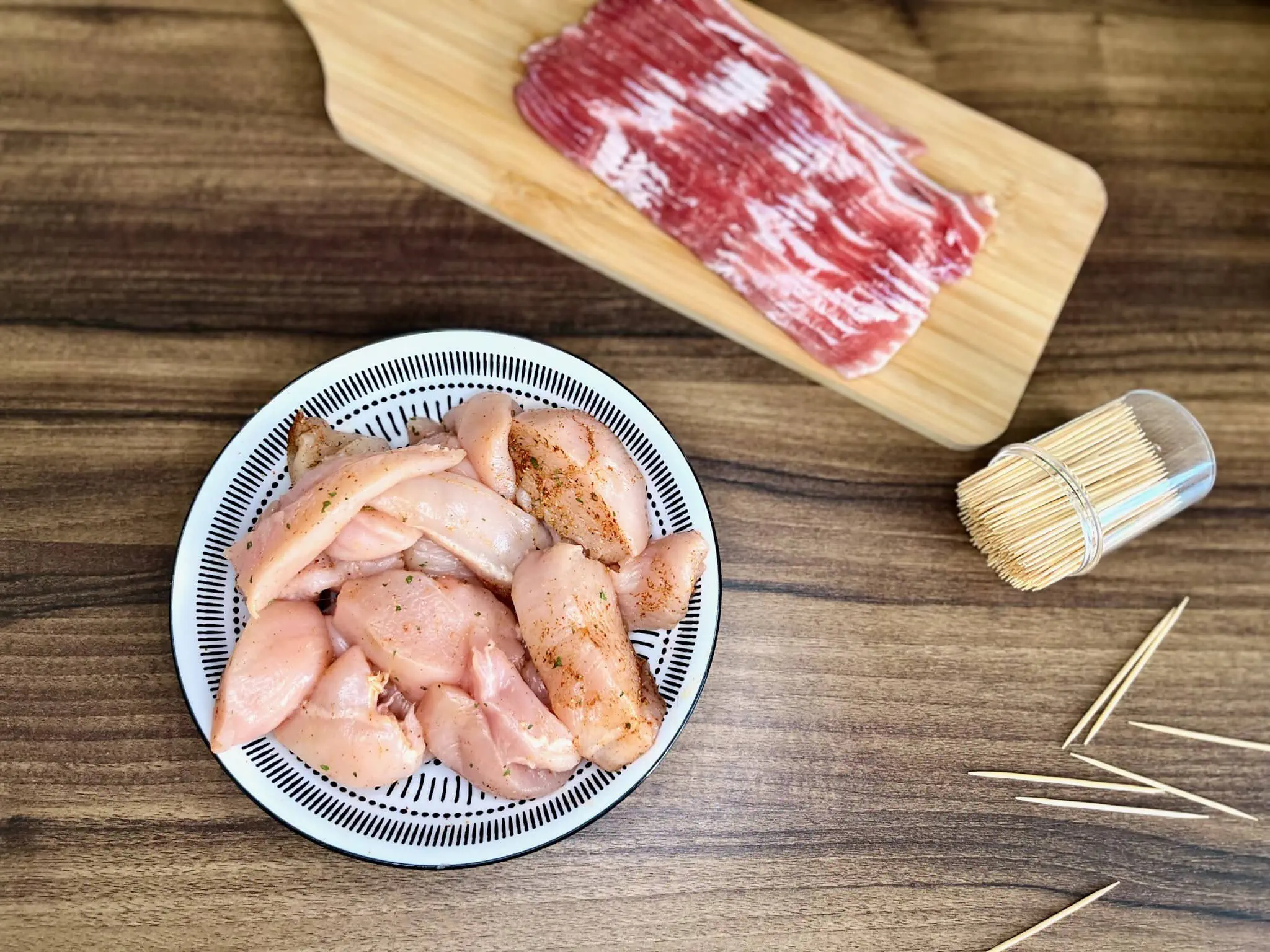 Chunks of chicken seasoned with spices rest in a bowl, ready to be assembled into Bacon-Wrapped Chicken Bites