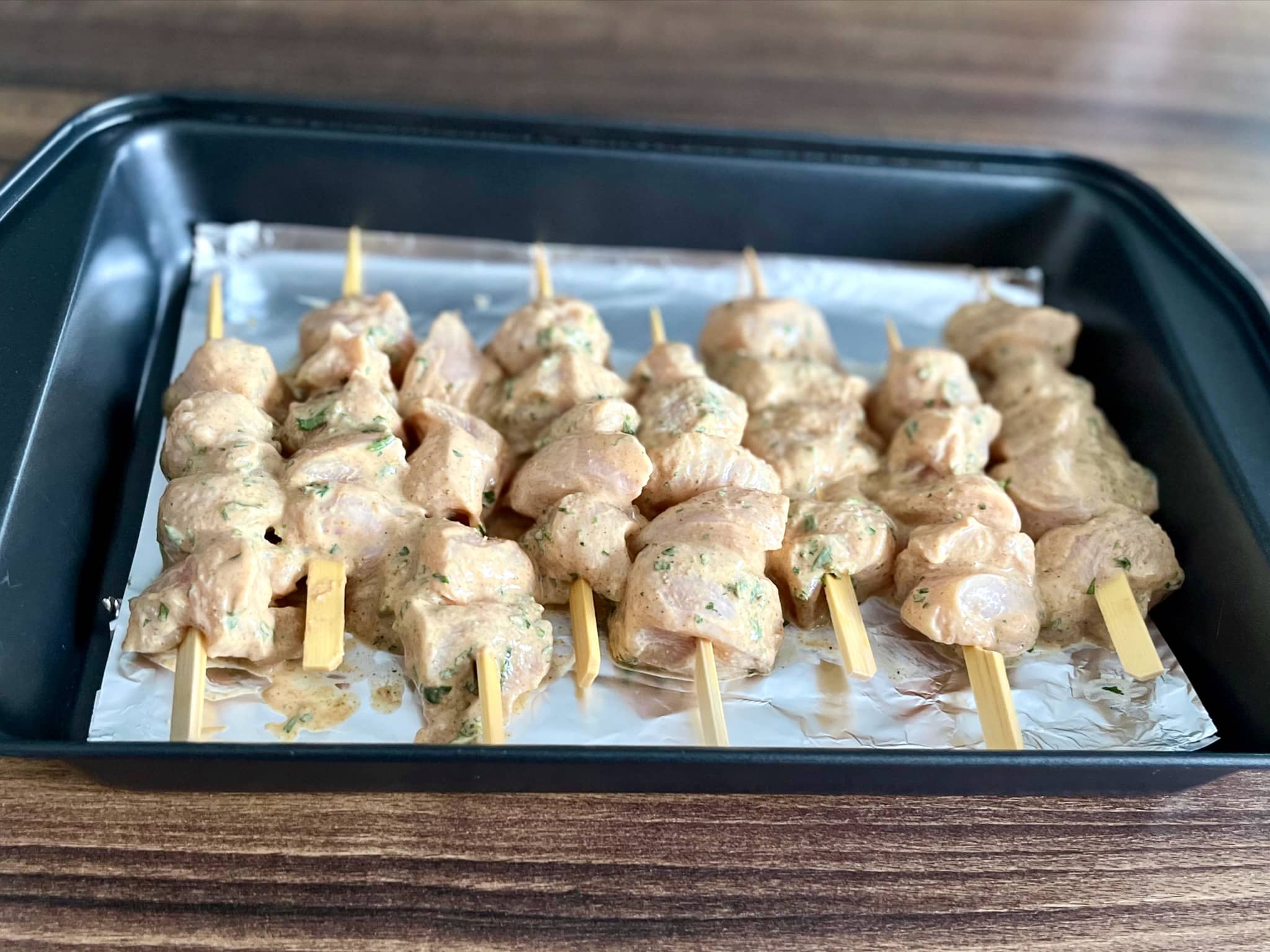 Chicken cubes threaded onto skewers, placed on in a baking tray lined with aluminium foil