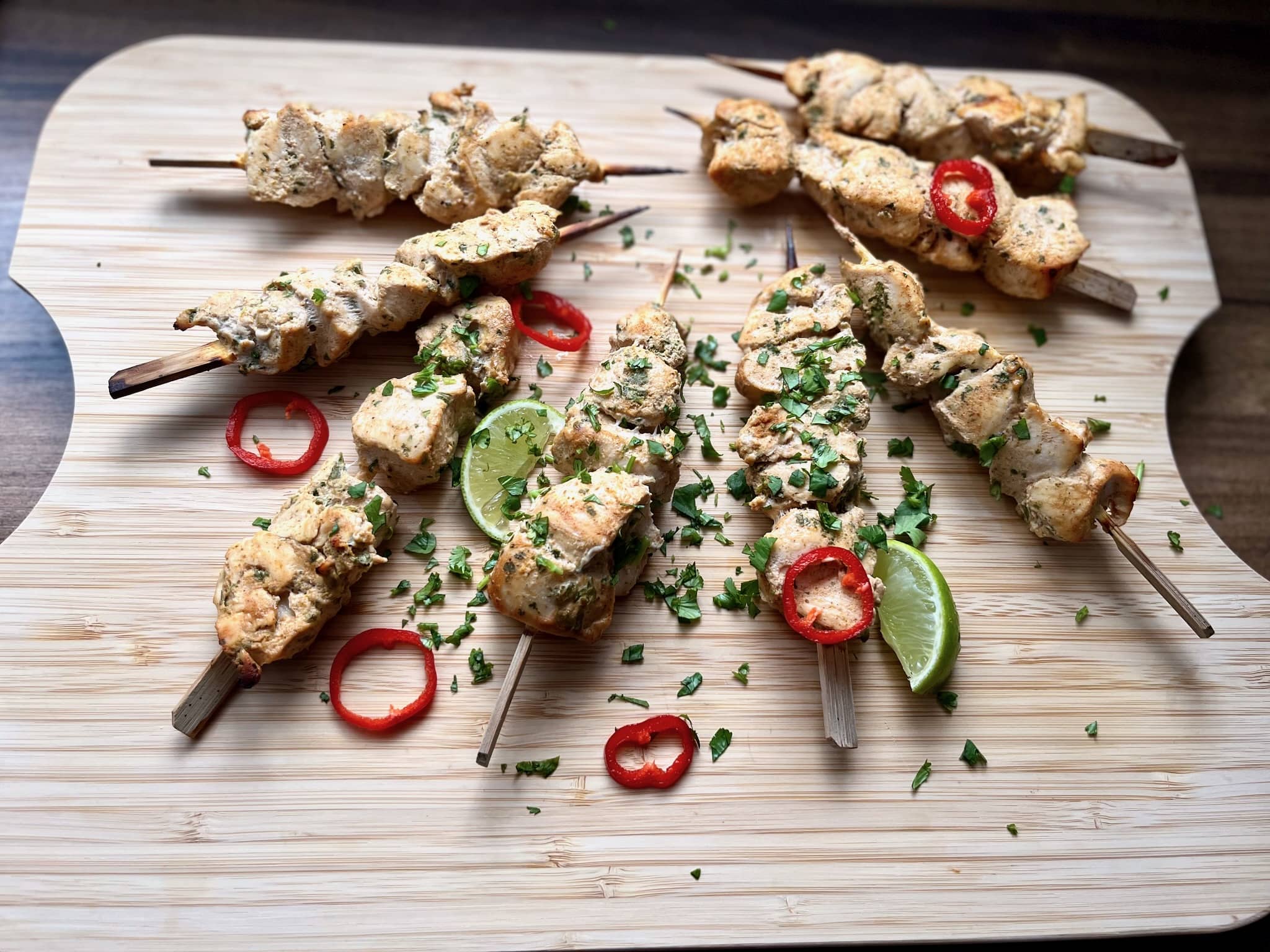 Juicy baked chicken tikka skewers, garnished with fresh coriander, red chilli pepper, and lime, served on a chopping board