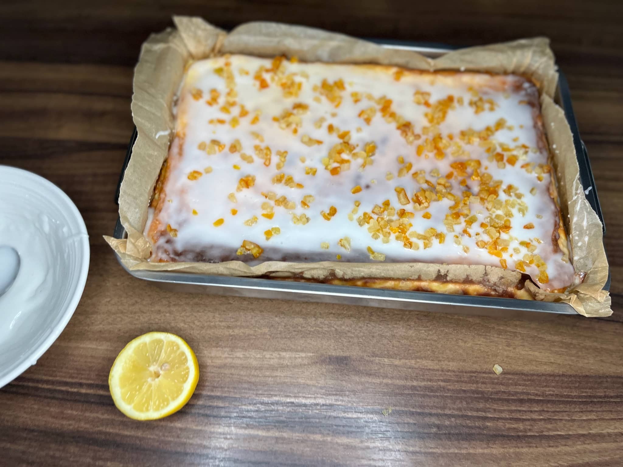 Cheesecake covered with icing and orange and lemon peel still in a tray
