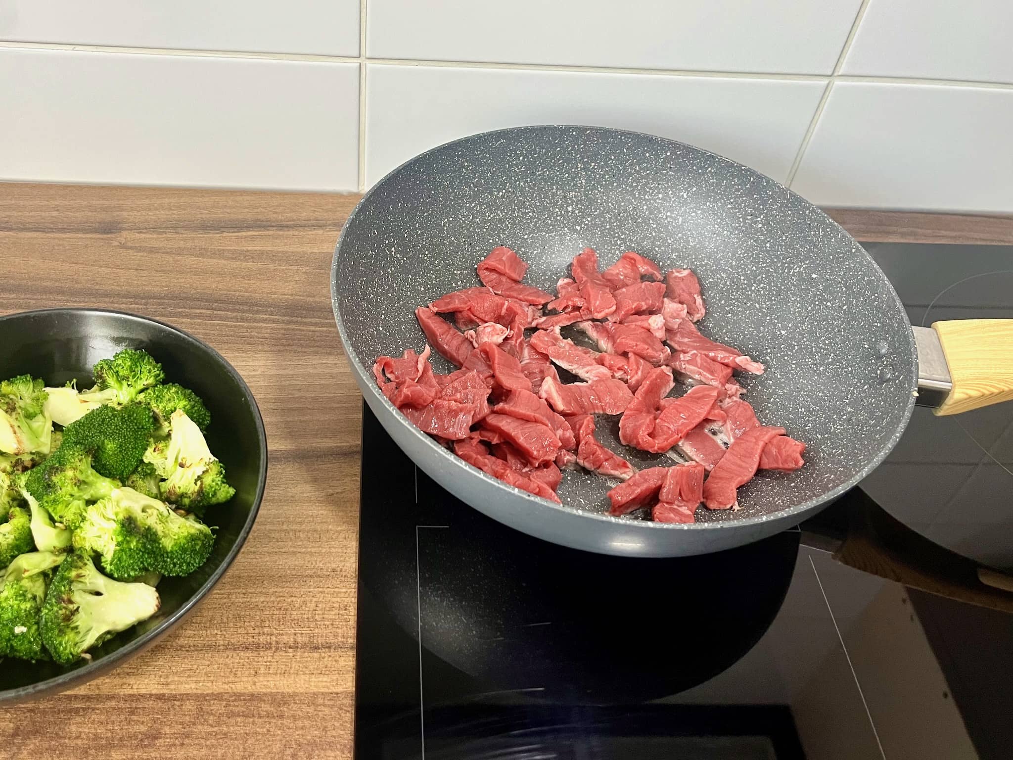 Beef slices frying in a pan with broccoli florets in a bowl on the side