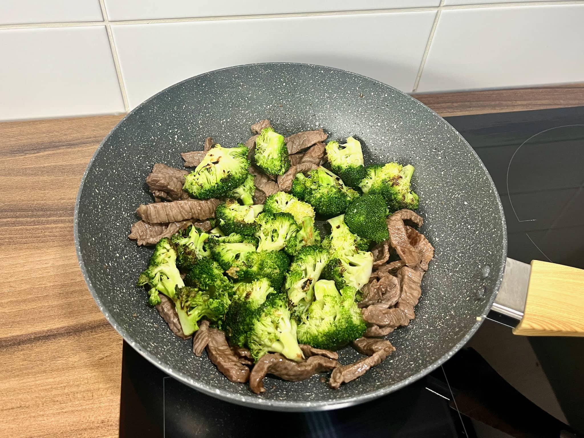 Broccoli florets added on top of beef slices in a pan