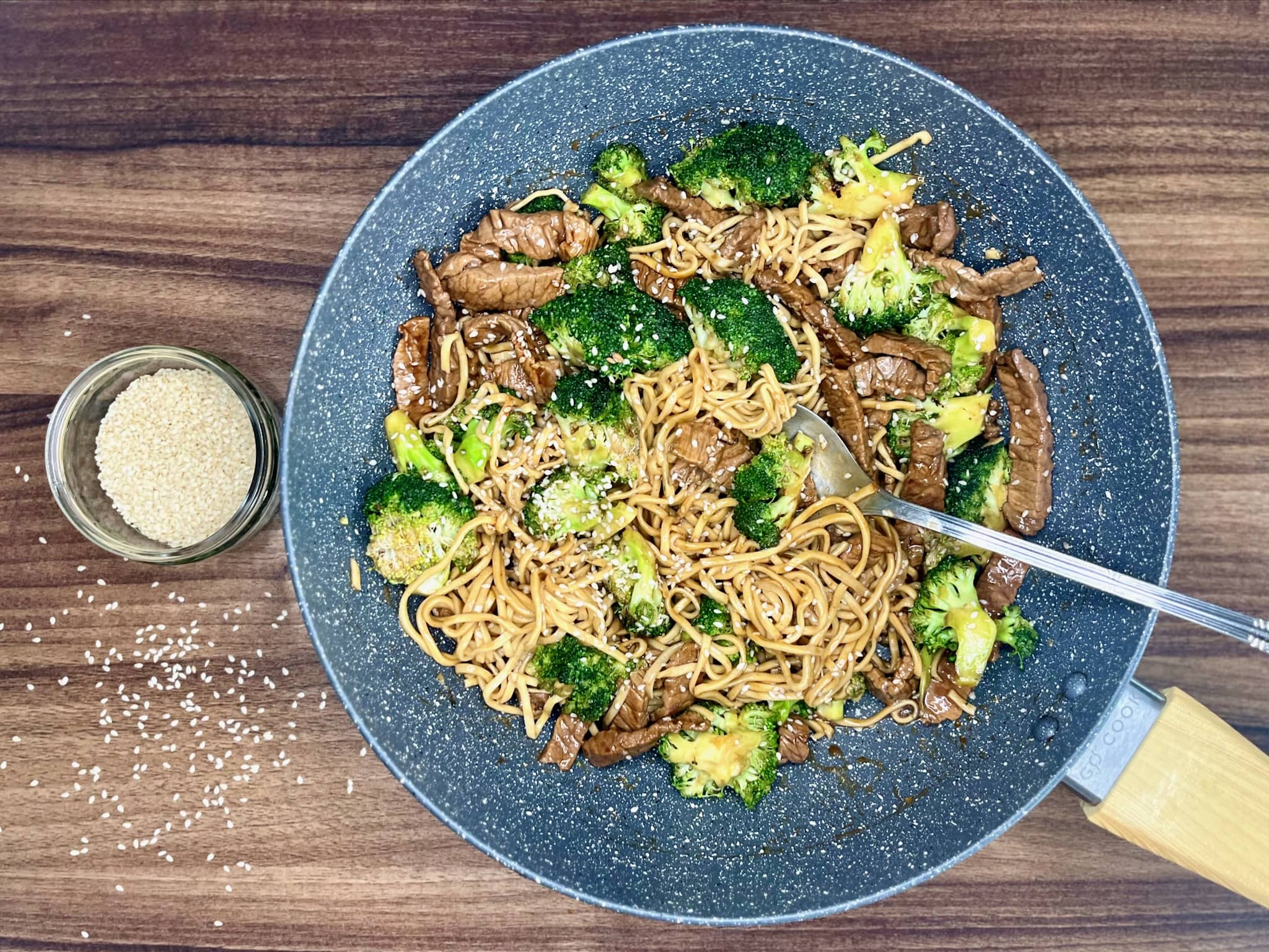 Beef and broccoli with egg noodles in a pan, sprinkled with sesame seeds