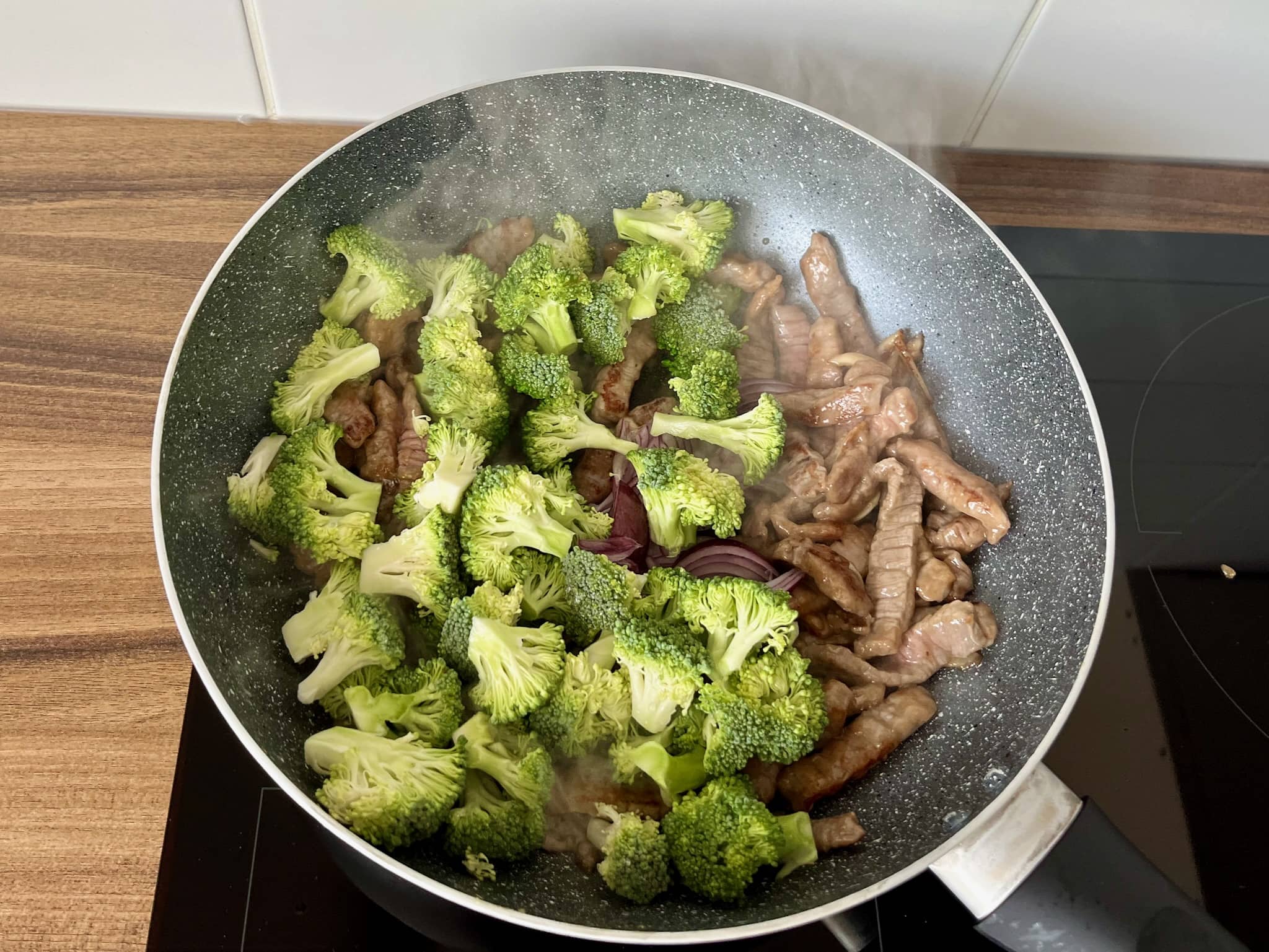Fried beef in a pan with broccoli florets on top