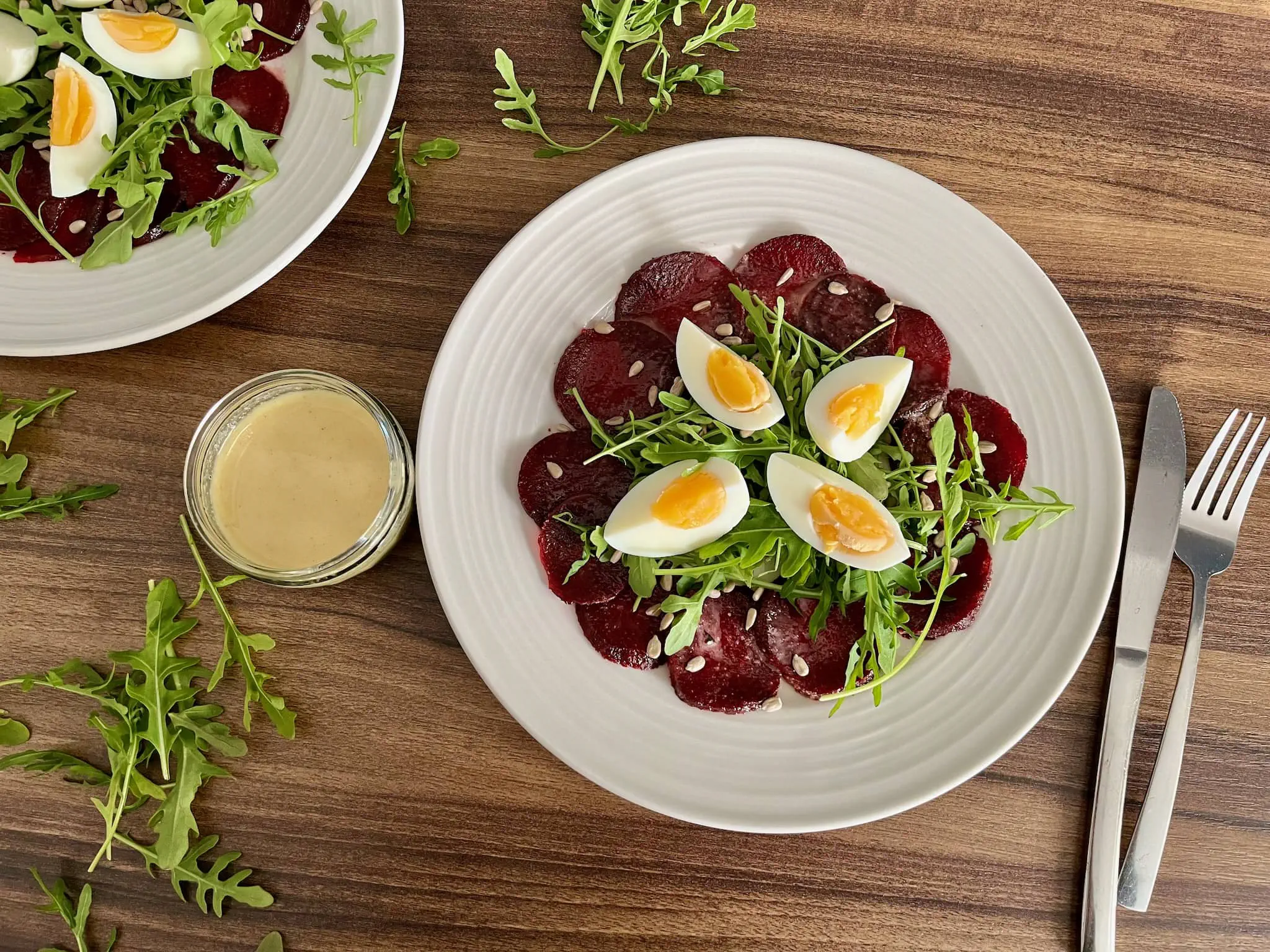 Carpaccio z buraka na talerzu z rukolą i jajkami, sos w sosjerce
