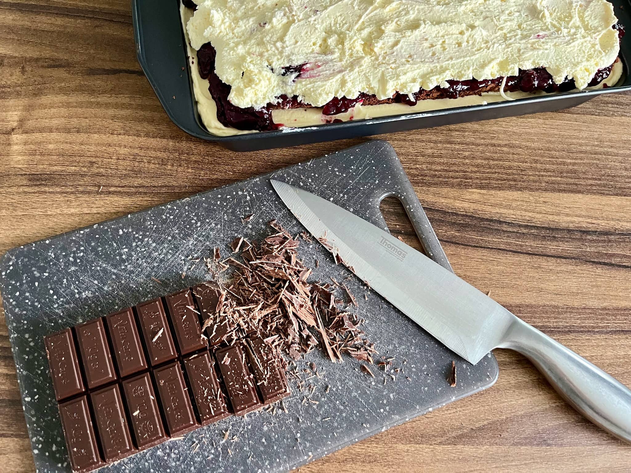 Blackcurrant cake in a tray and chopped chocolate on the chopping tray ready for decorating