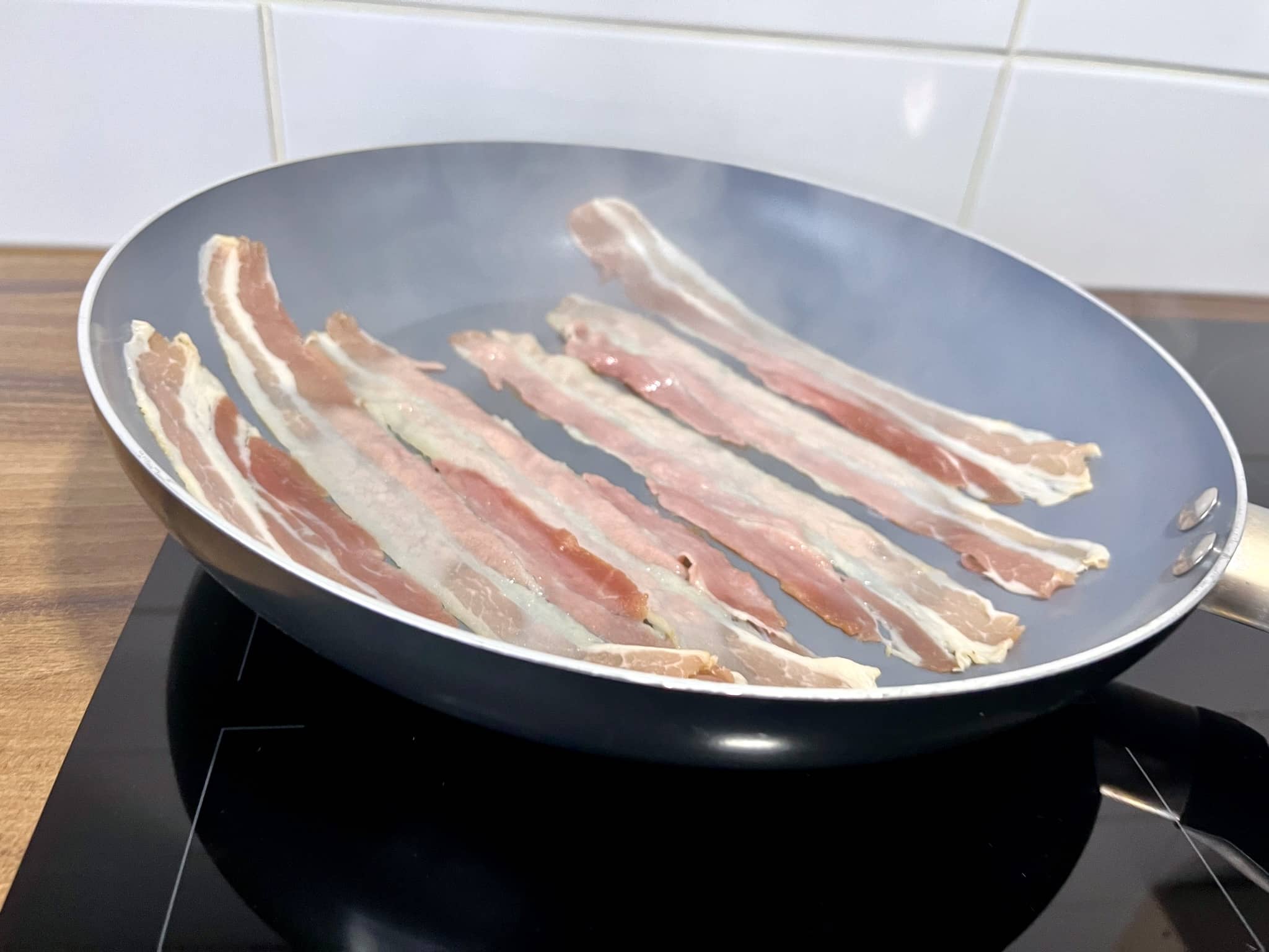 Smoked pancetta rashers are frying in a skillet