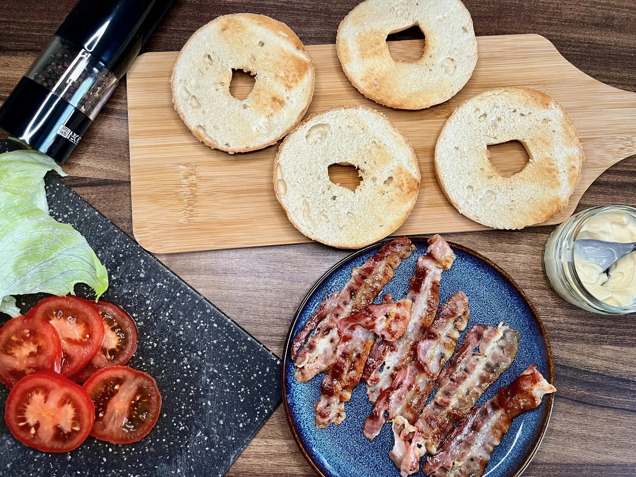 Toasted bagles, fried bacon and rest of ingredients for BLT Bagel Sandwich on table top
