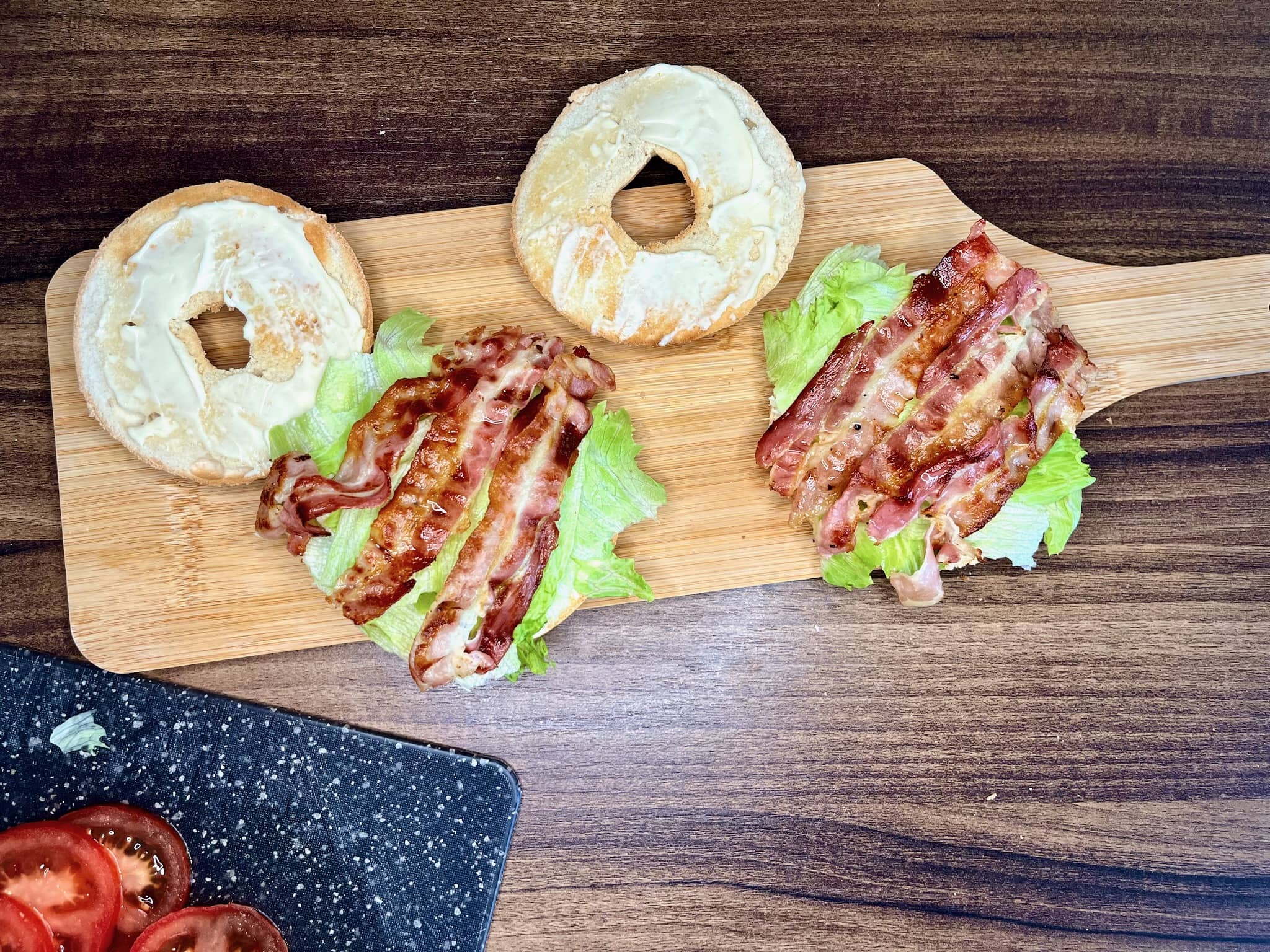 Toasted bagel halves, dressed with crisp lettuce and neatly arranged bacon slices, rest invitingly on a wooden chopping board
