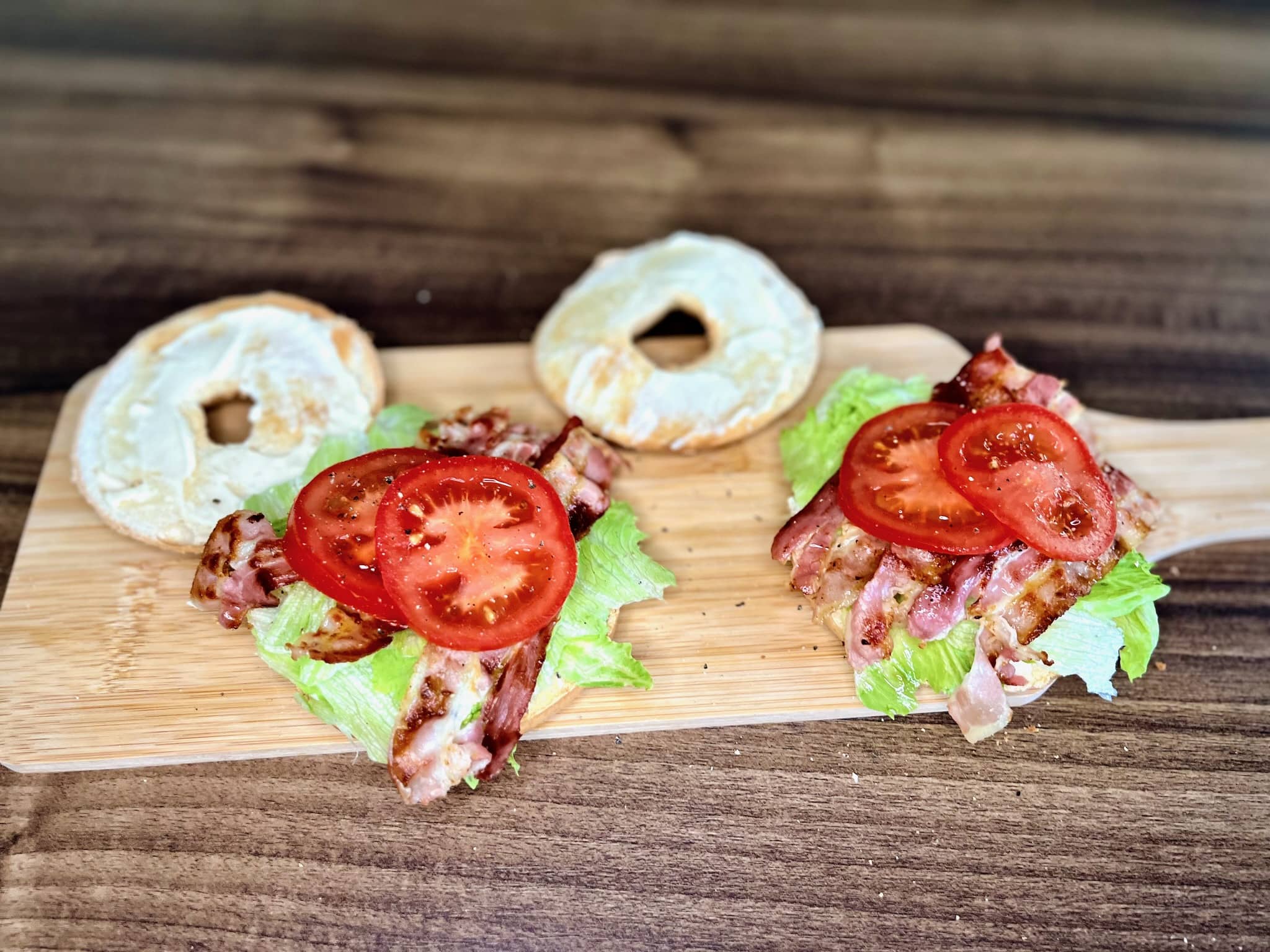 Slices of juicy tomato join the BLT party on toasted bagels, sprinkled with freshly ground black pepper