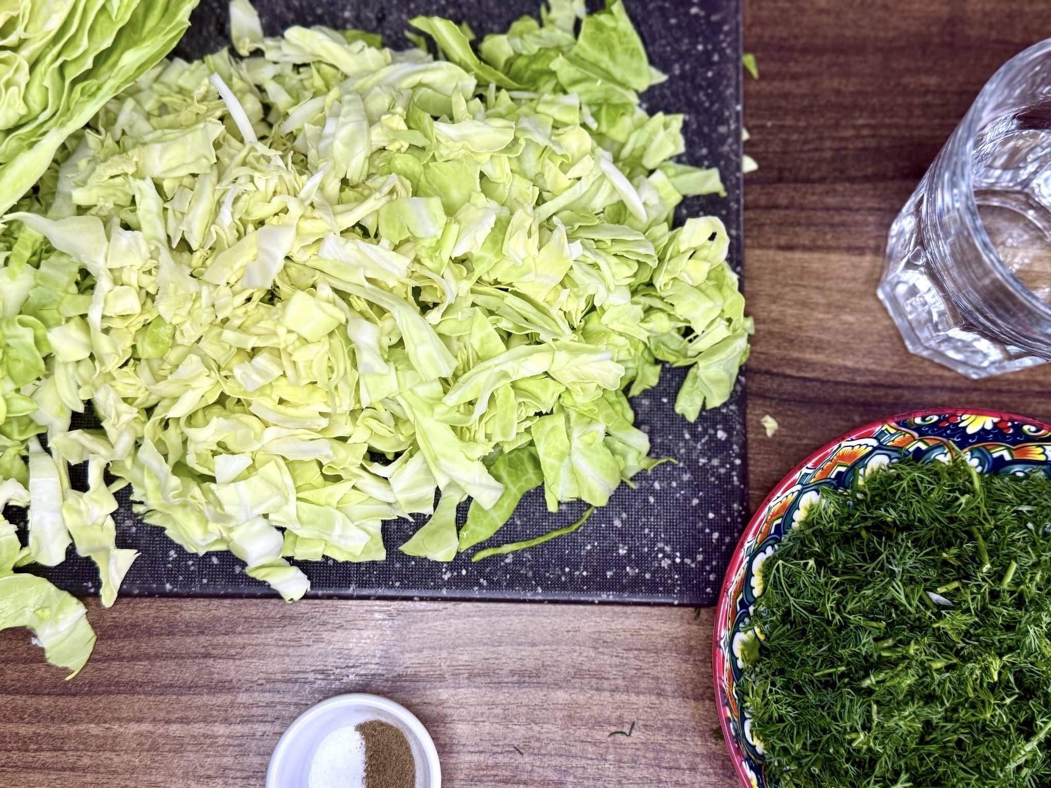 Shredded cabbage on a chopping board and chopped dill in a bowl