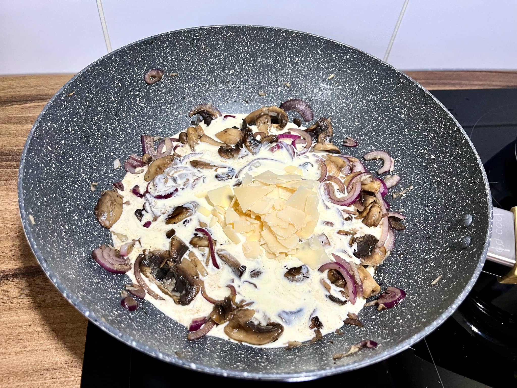 Double cream and Parmesan shavings added to mushrooms and onion in a pan