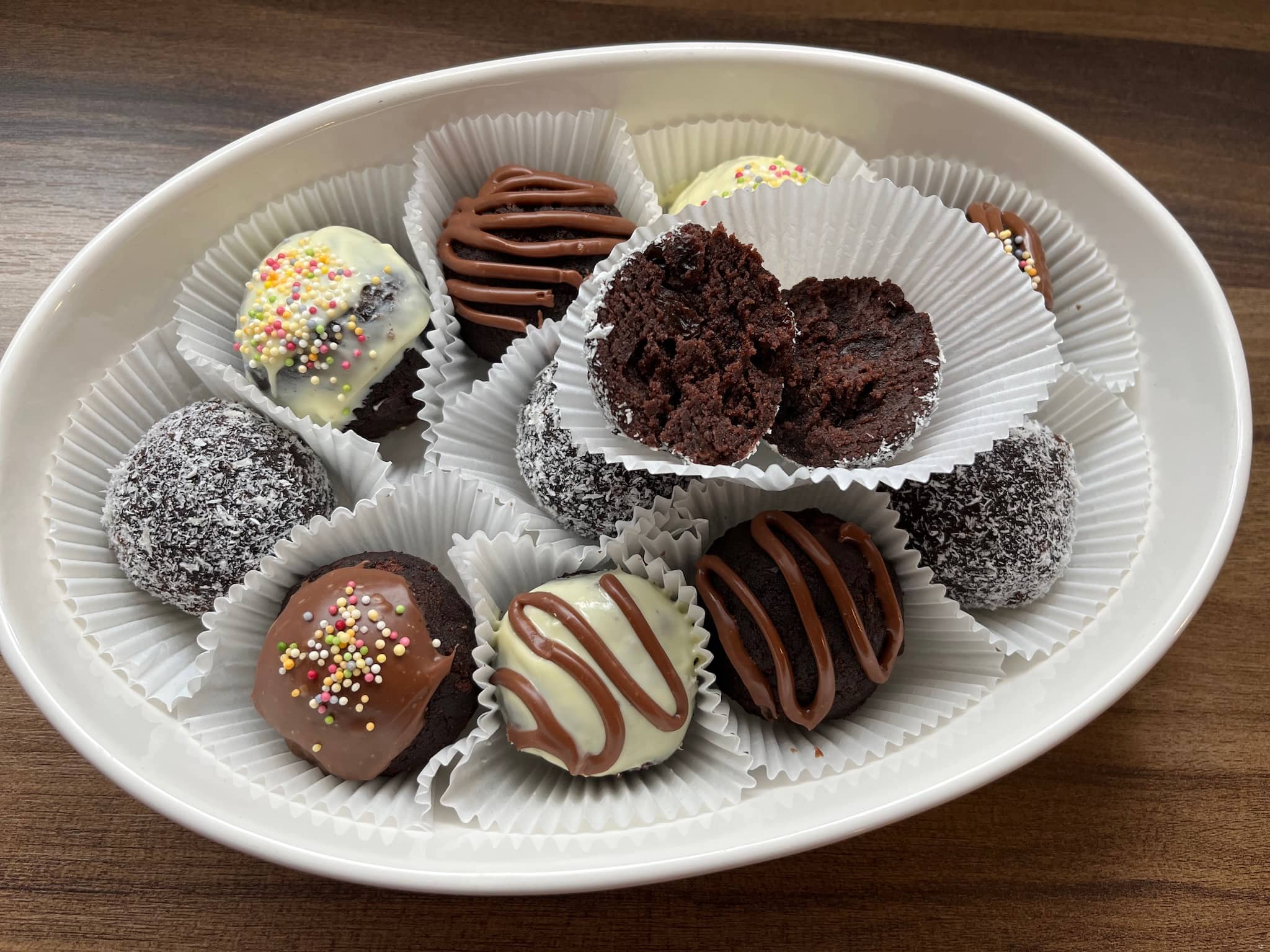 Decorated cake balls in muffin cases on a plate with one broken in half