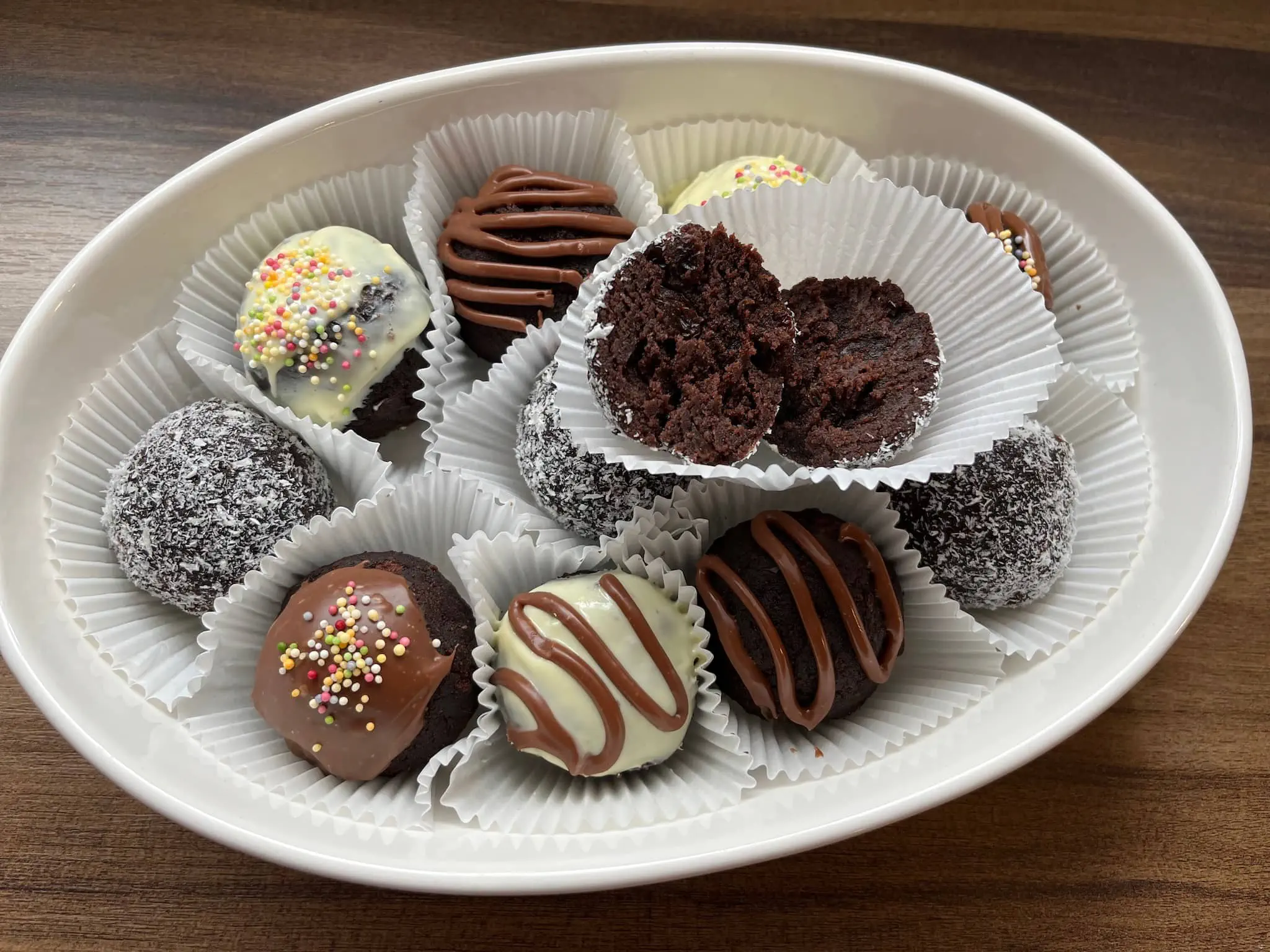Decorated cake balls in muffin cases on a plate with one broken in half