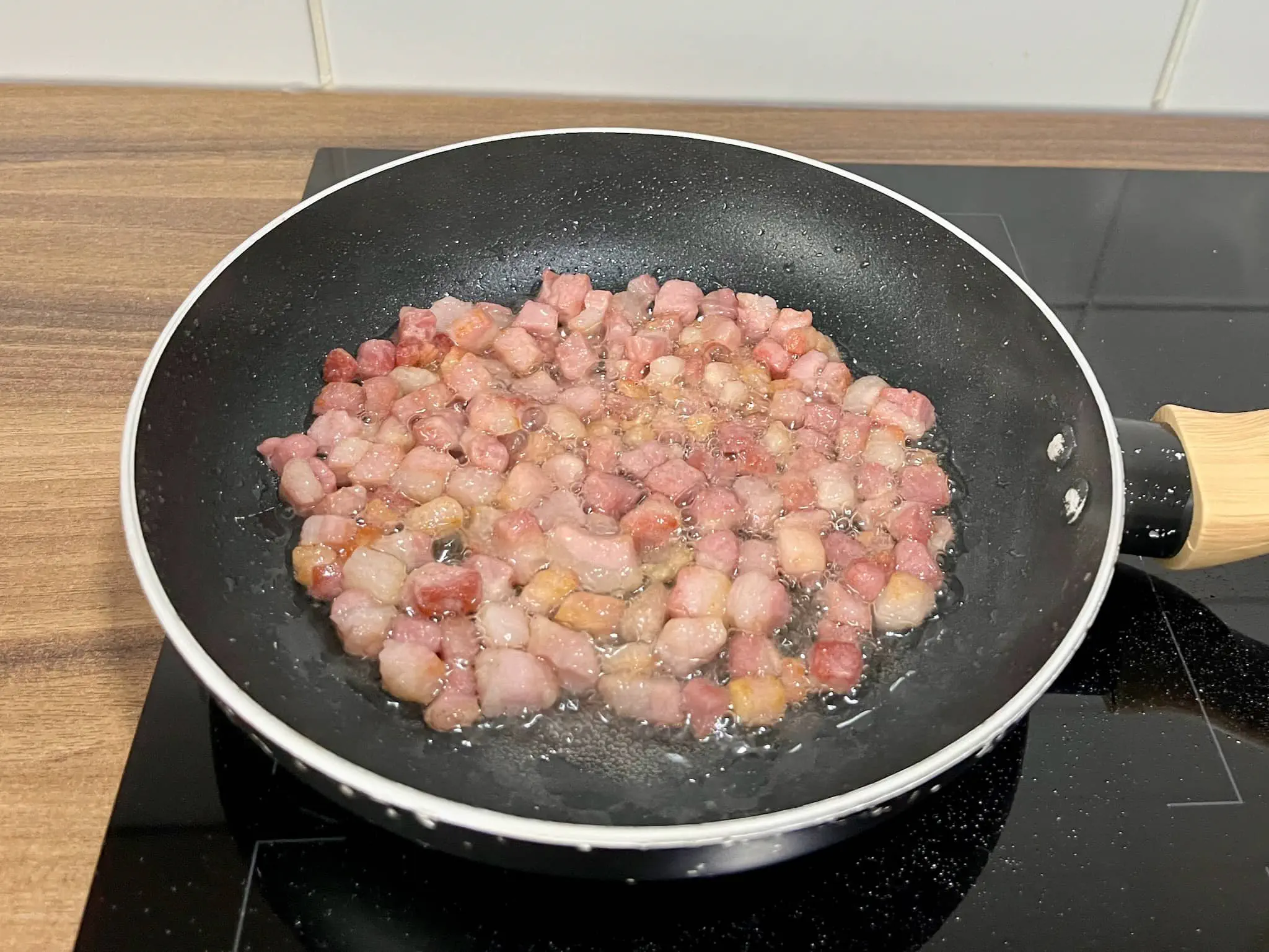 Podsmażona wędzona pancetta w kostkach na patelni