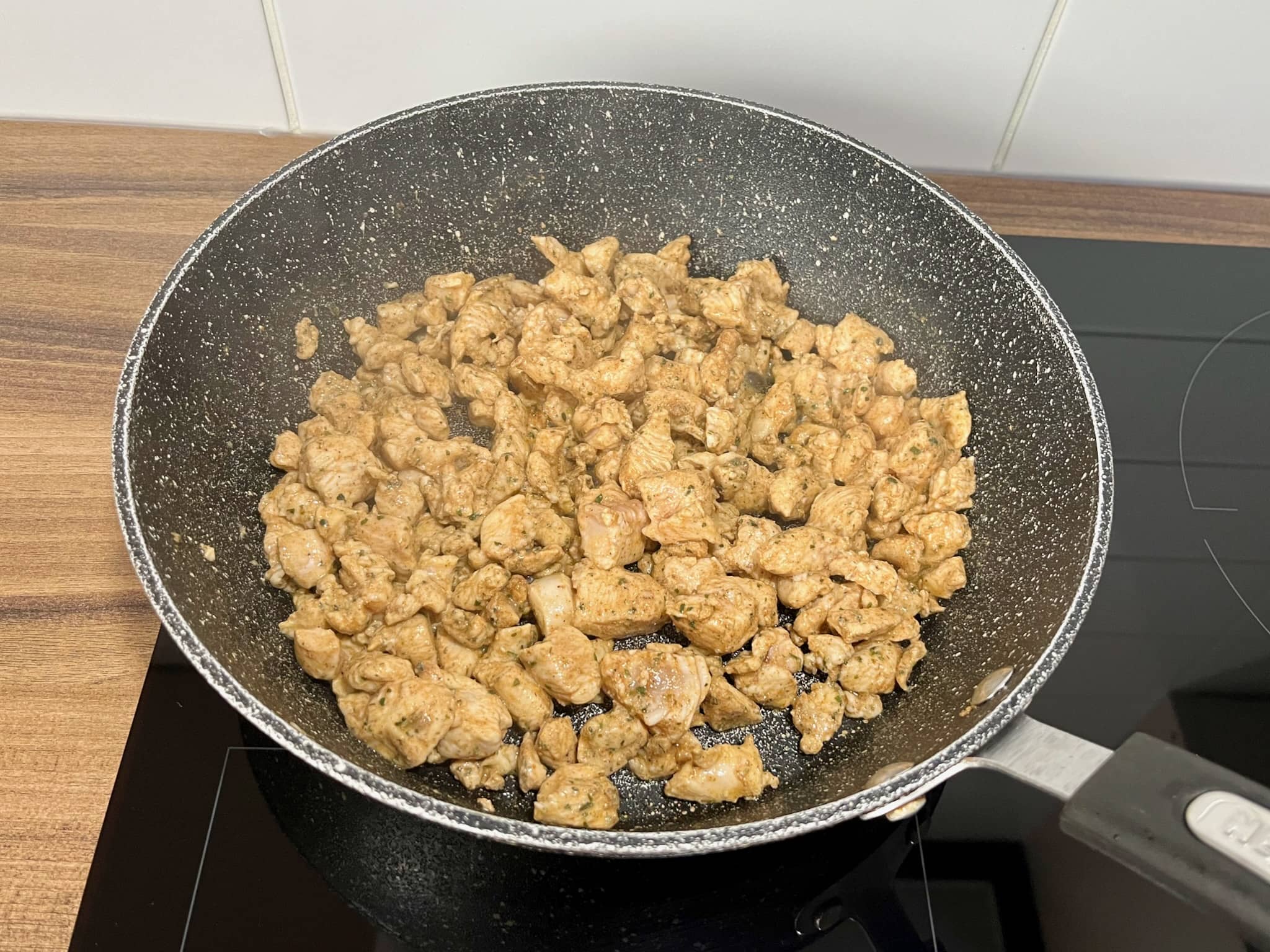 Chicken breast cubes frying in a large pan