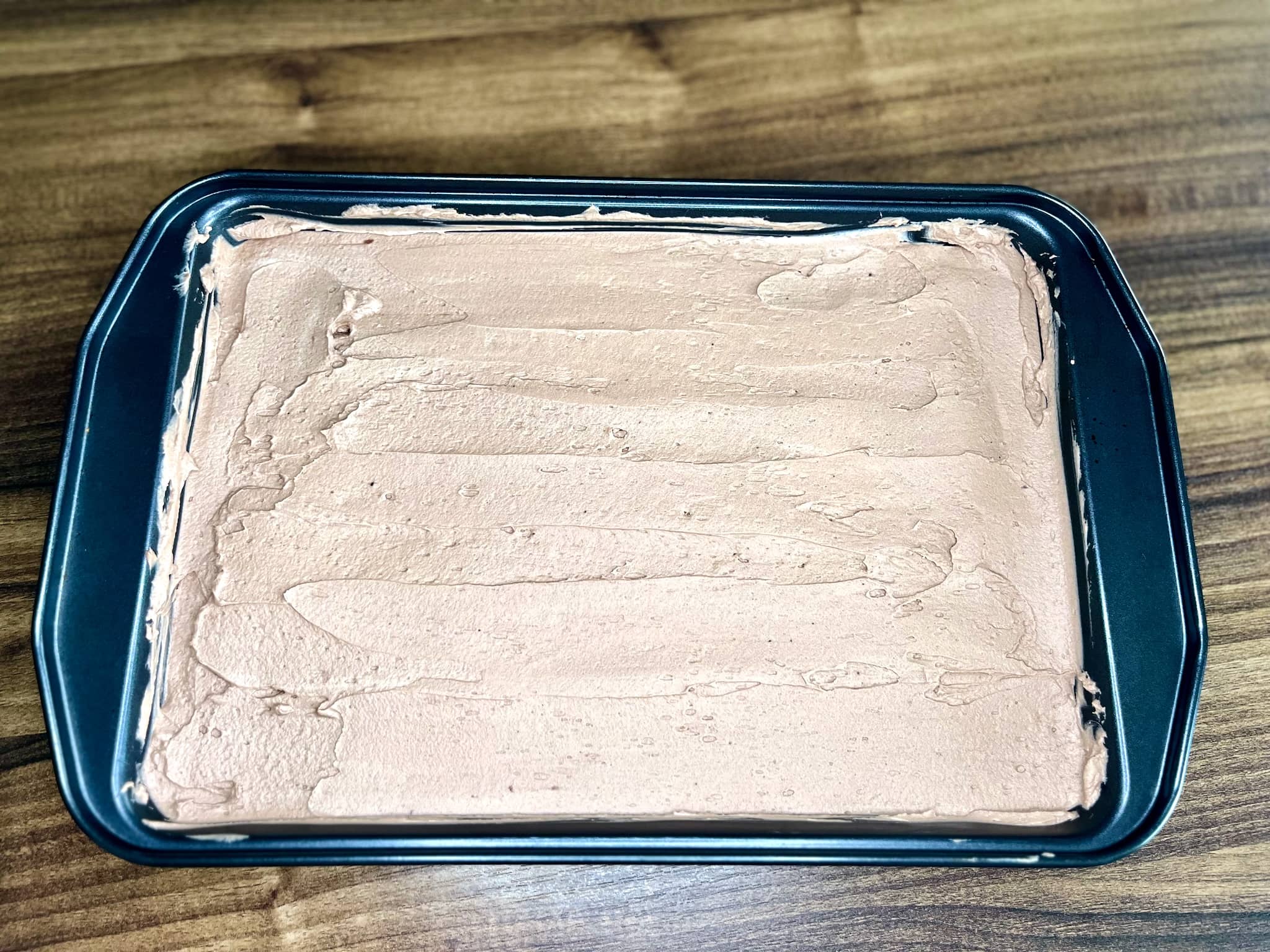 Chocolate filling spooned/poured onto the cake base in a tin
