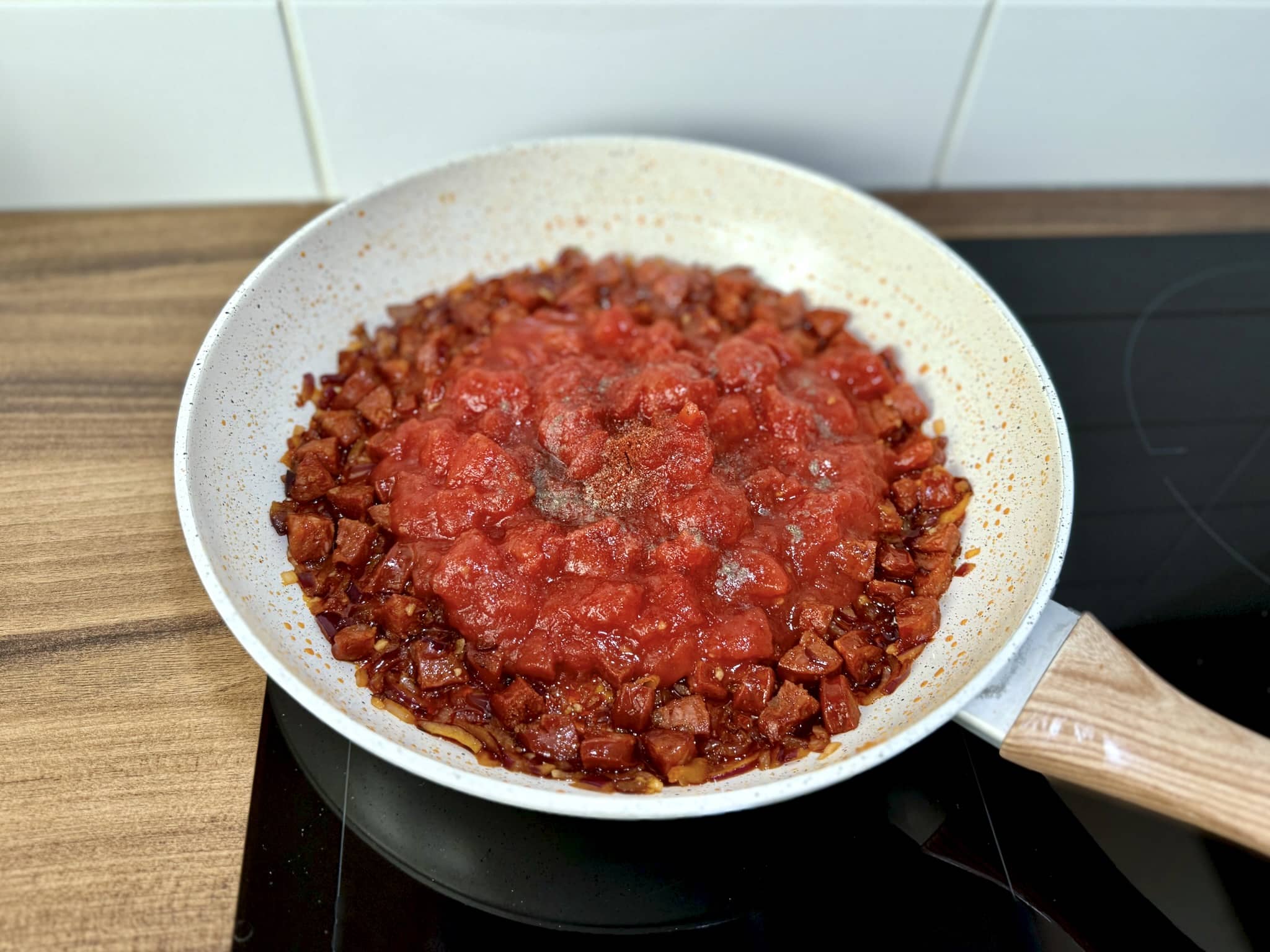 Usmażone Chorizo, cebula i czosnek z dodanymi pomidorami i przyprawami na patelni