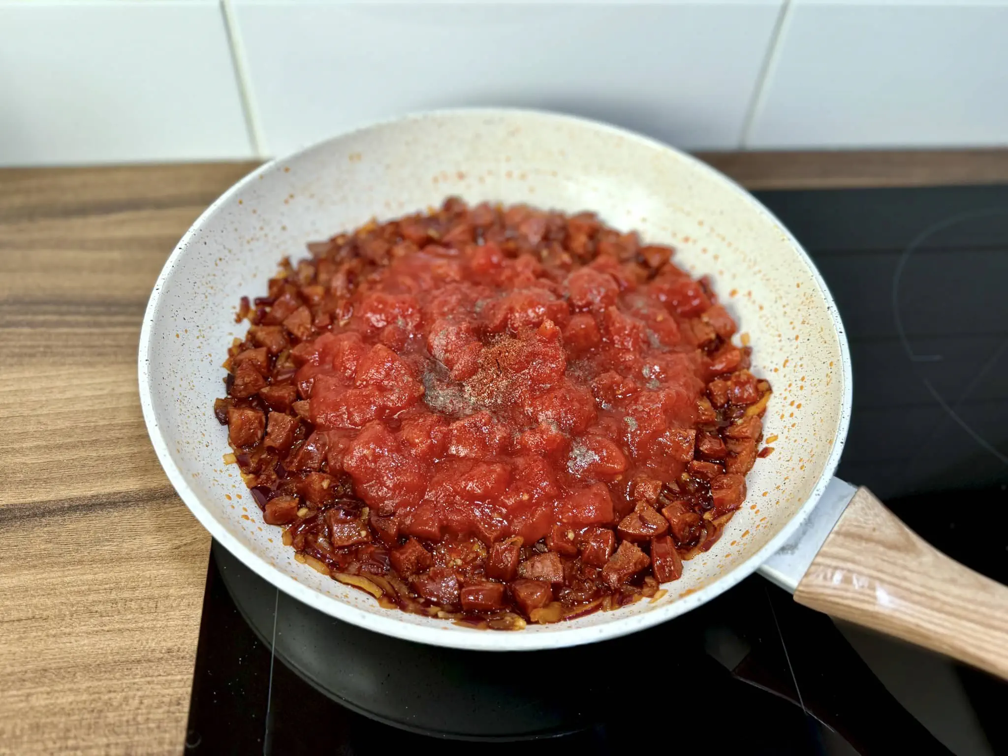 Usmażone Chorizo, cebula i czosnek z dodanymi pomidorami i przyprawami na patelni