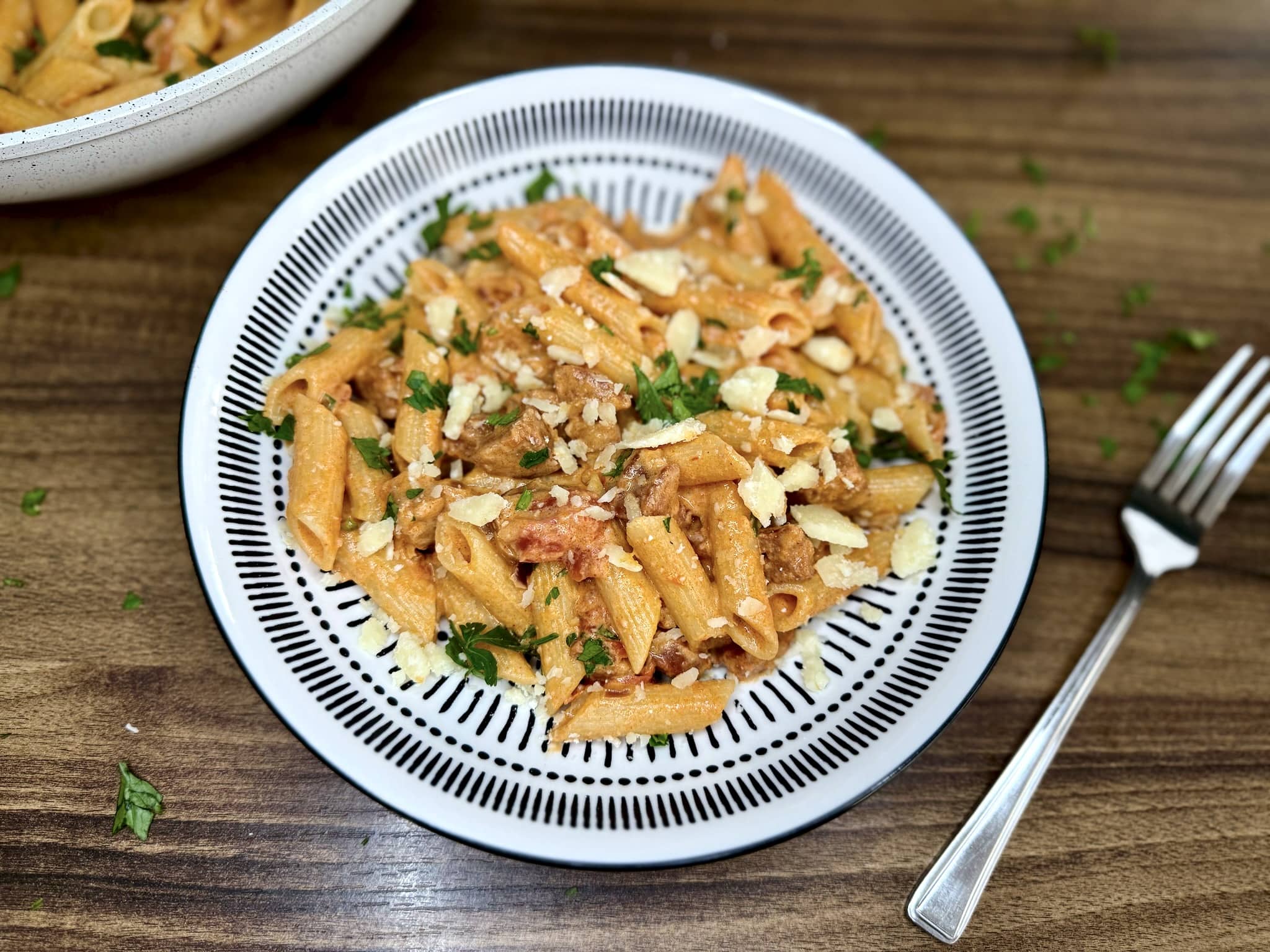 Porcja Makaronu z Chorizo w Kremowym Sosie Pomidorowym na talerzu posypana parmezanem