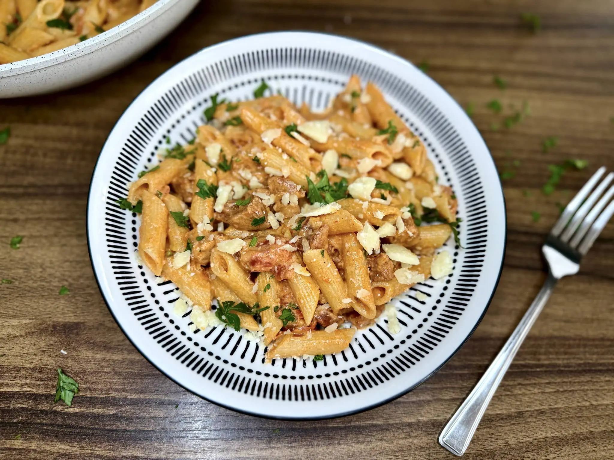 Porcja Makaronu z Chorizo w Kremowym Sosie Pomidorowym na talerzu posypana parmezanem