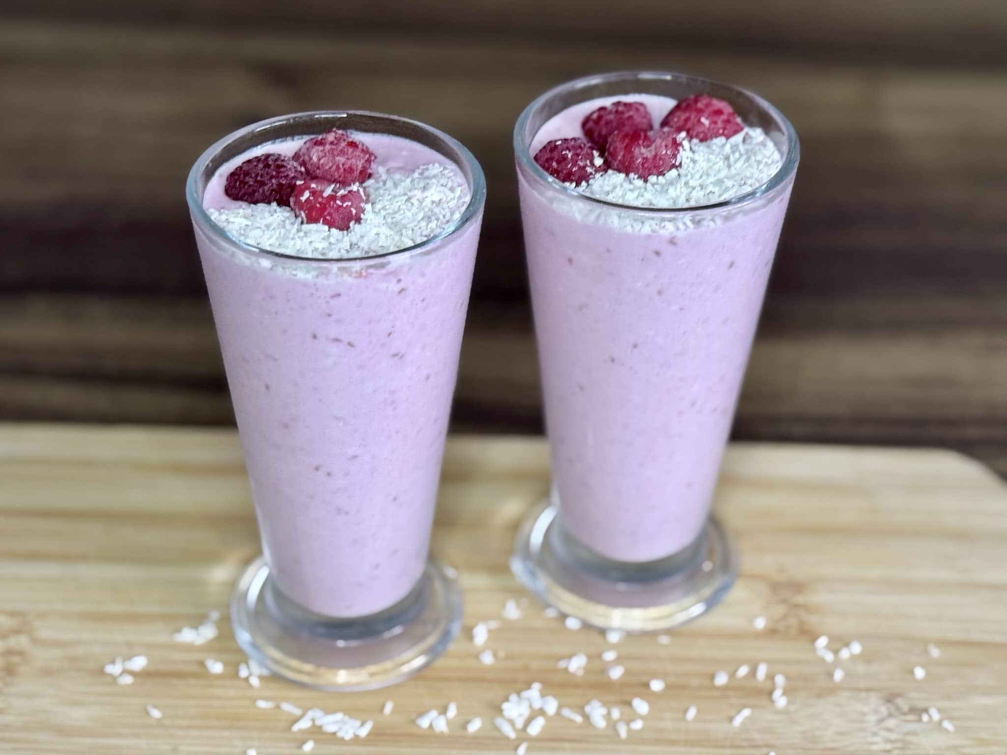 Ready Coconut and Raspberry Smoothie in tall glasses, decorated with desiccated coconut and raspberries