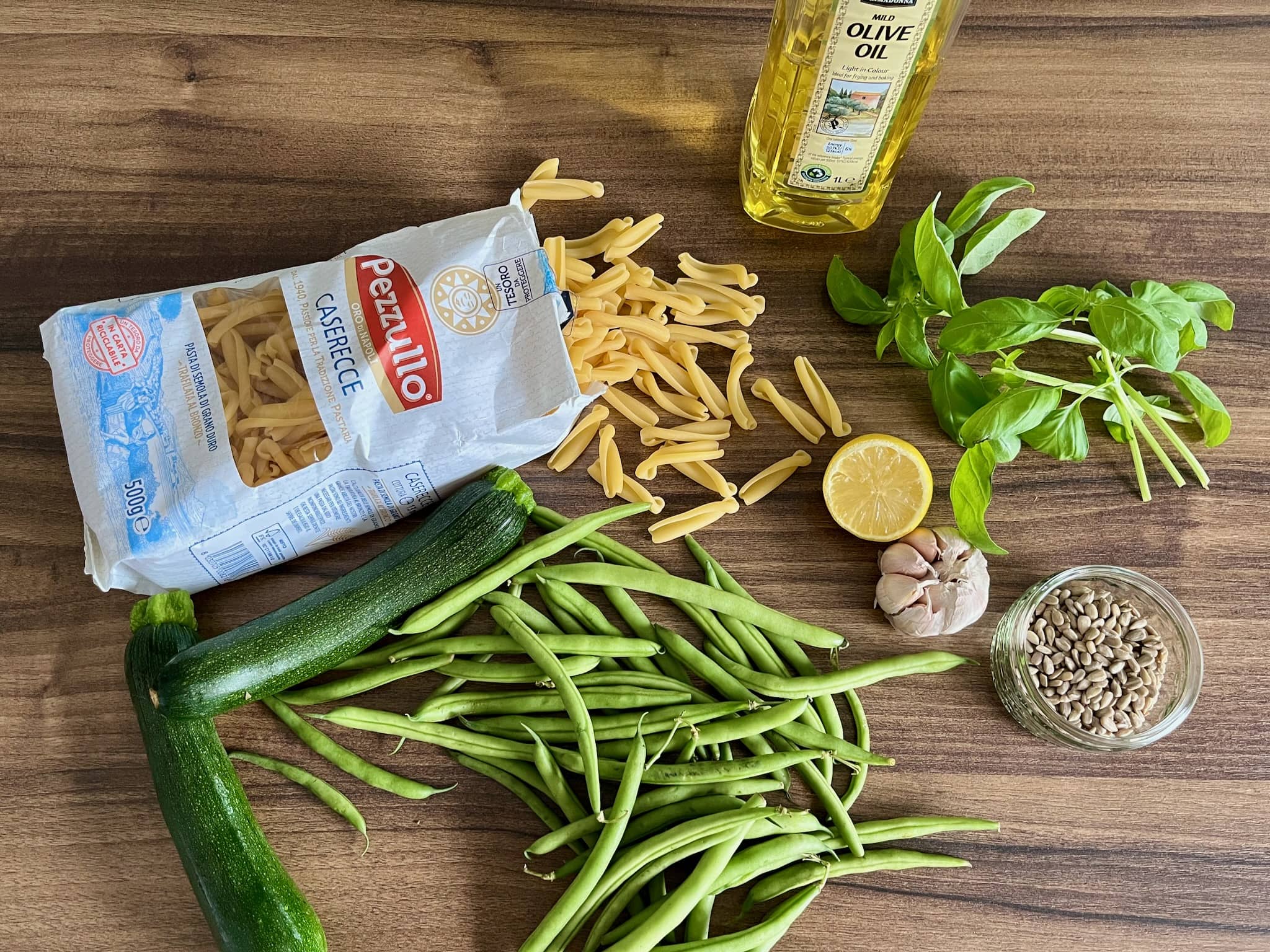 Ingredients on a table, pasta, olive oil, basil, courgette, green beans lemon, garlic and sunflower seeds