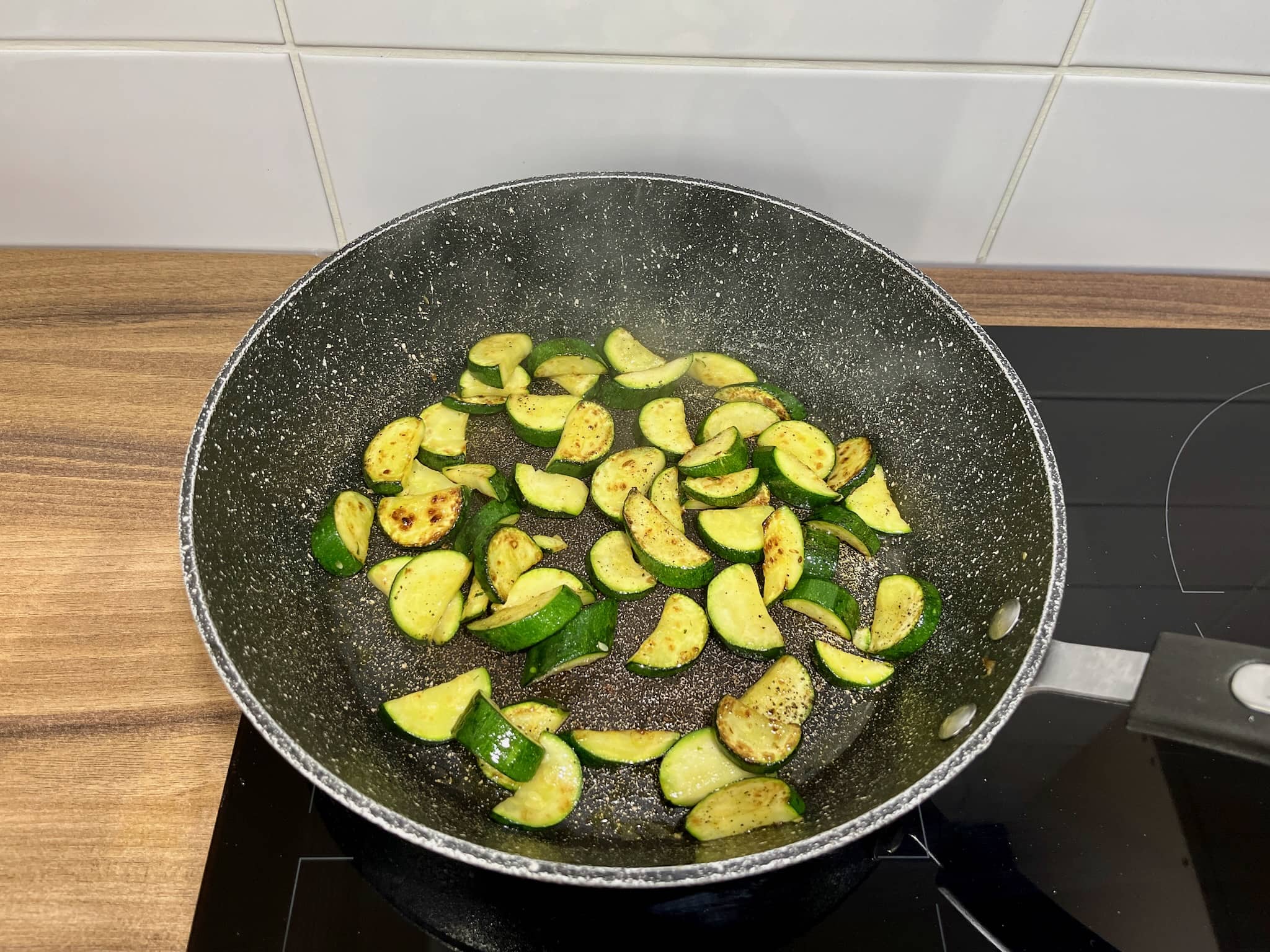 Courgette in pieces fried in a pan with salt and pepper