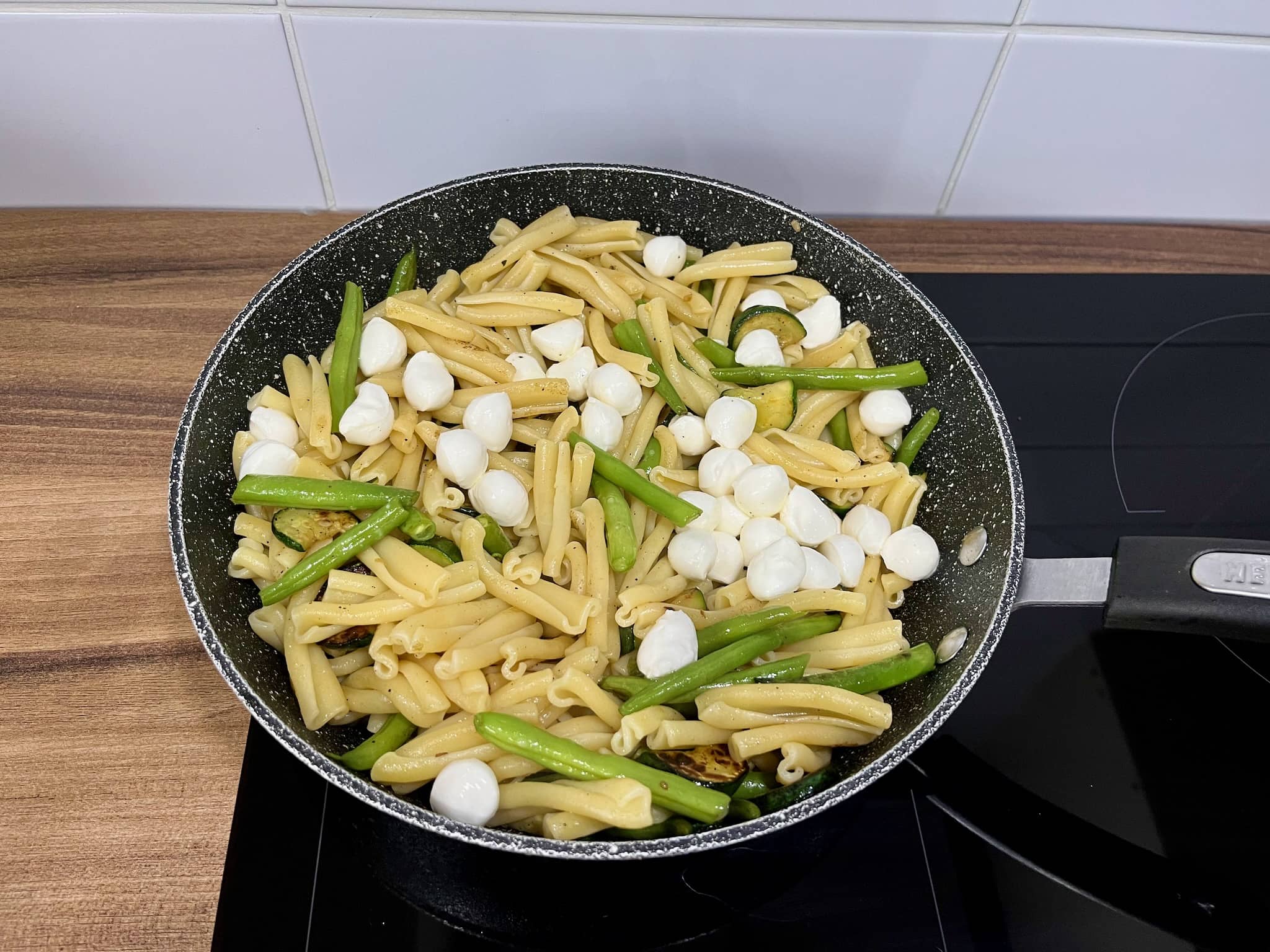 Courgette and green beans together with pasta and mozzarella in a pan