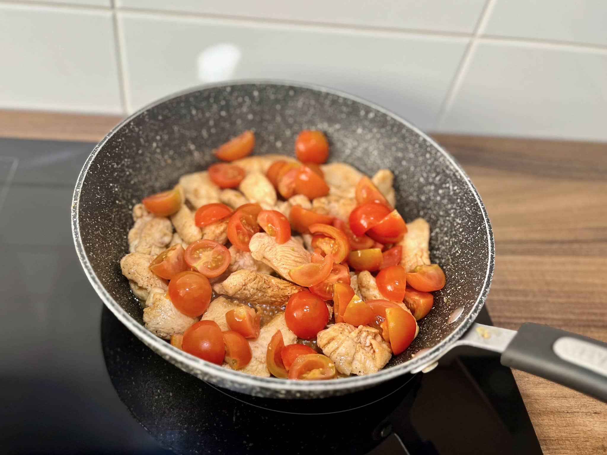 Golden brown fried chicken cooked in a large skillet, topped with juicy cherry tomatoes.