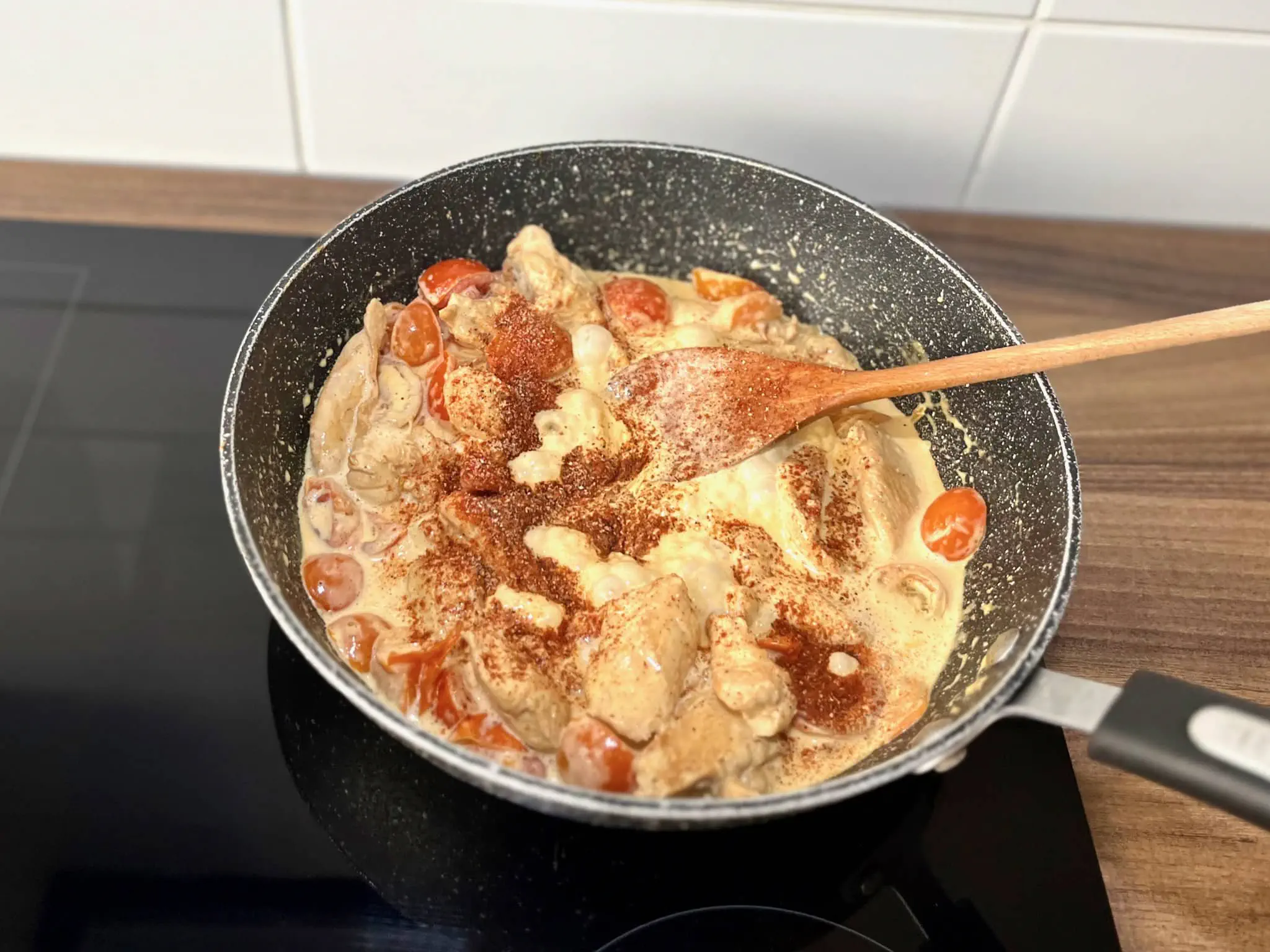 Chicken and cherry tomatoes seasoned with spices in a large skillet.