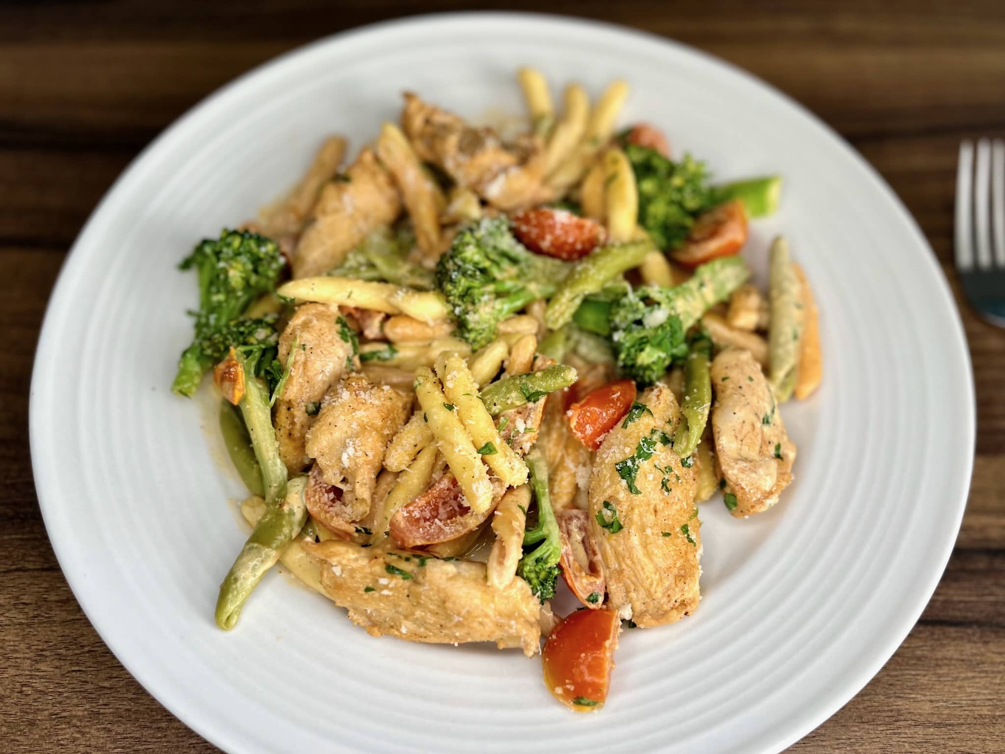 A generous portion of creamy chicken pasta with cherry tomatoes, served on a white plate.