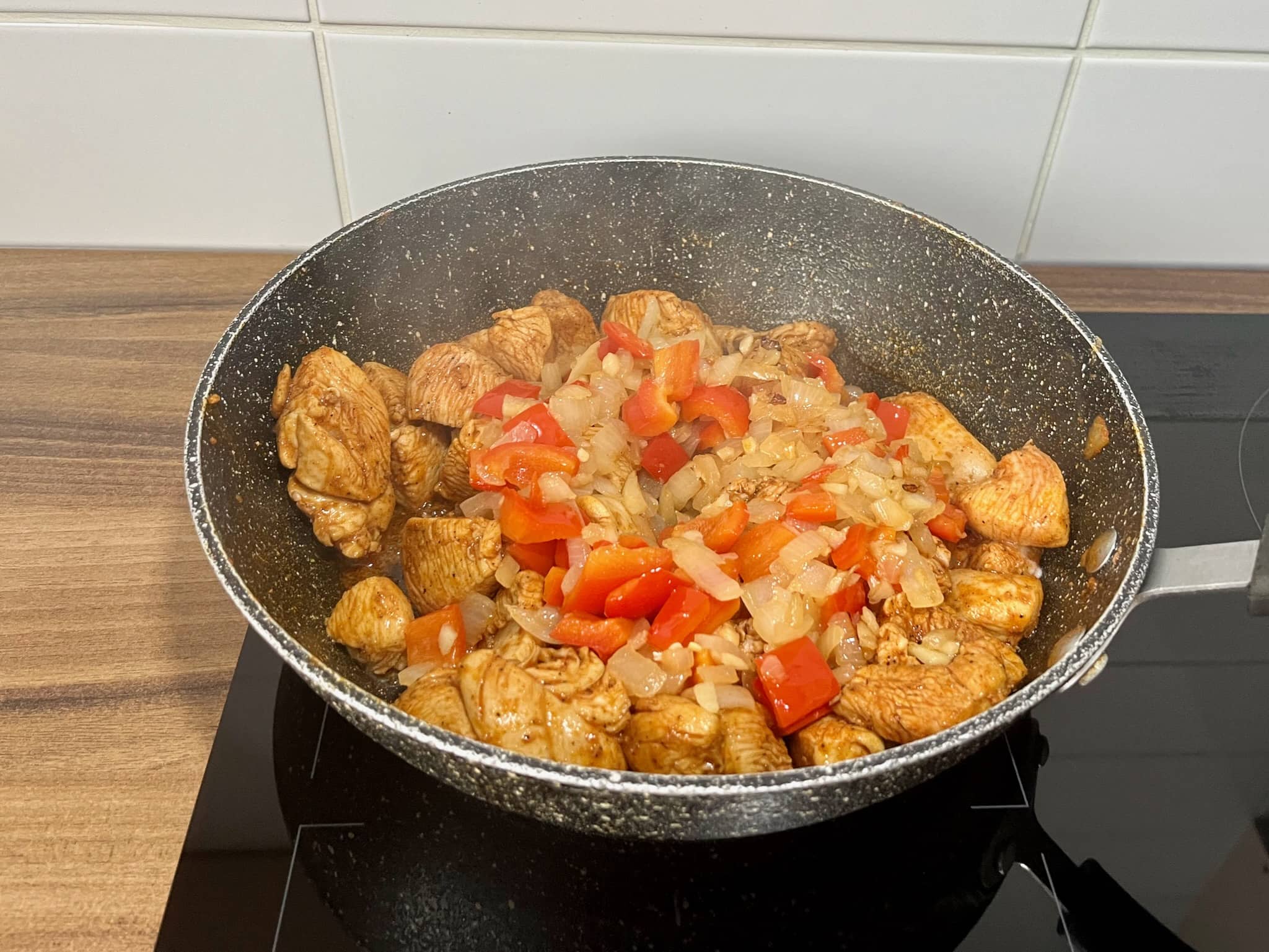 Diced chicken frying in a pan with onion and pepper mix