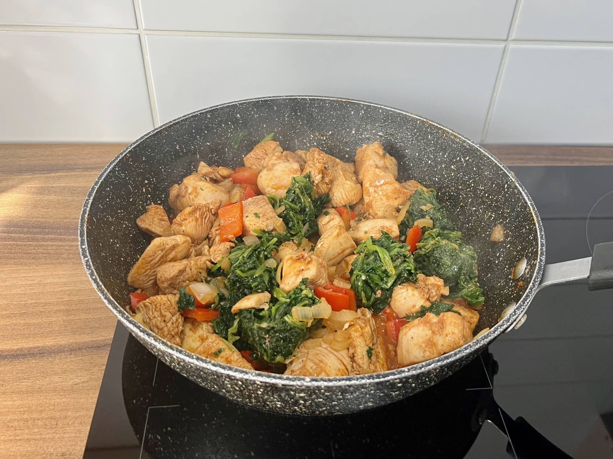Diced chicken frying in a pan with onion, pepper and spinach