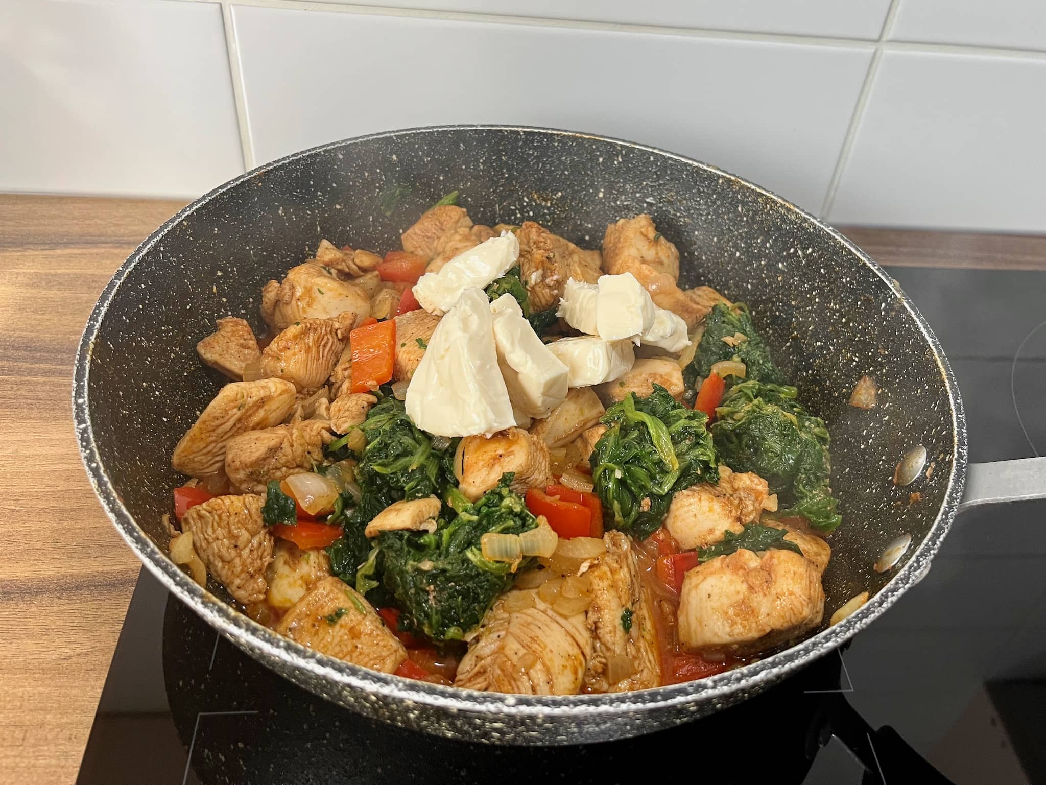 Diced chicken frying in a pan with onion, pepper, spinach and cheese triangles