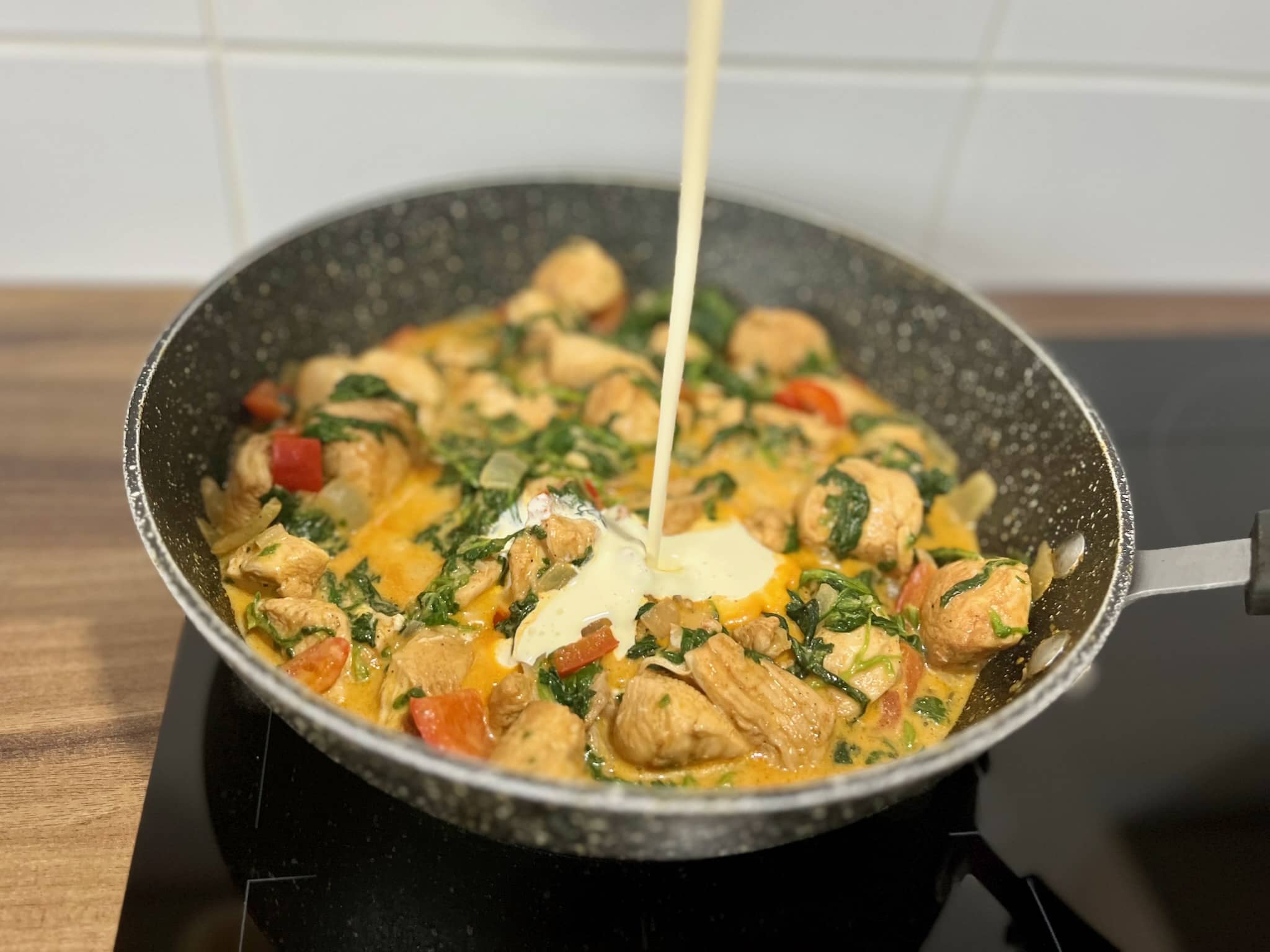 Pouring the double cream into a pan with chicken and vegetables
