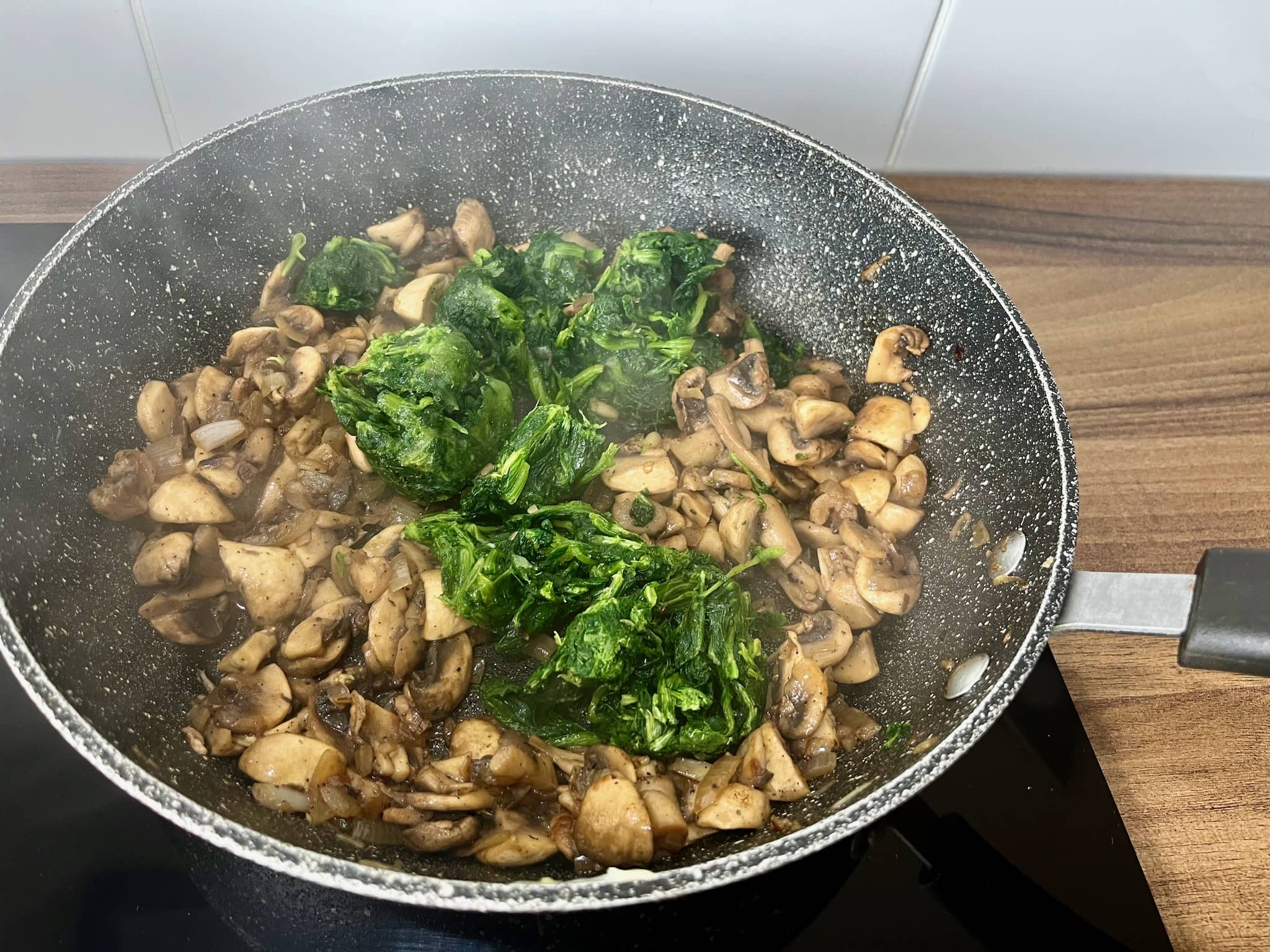 Mushrooms sizzling in a pan, topped with spinach