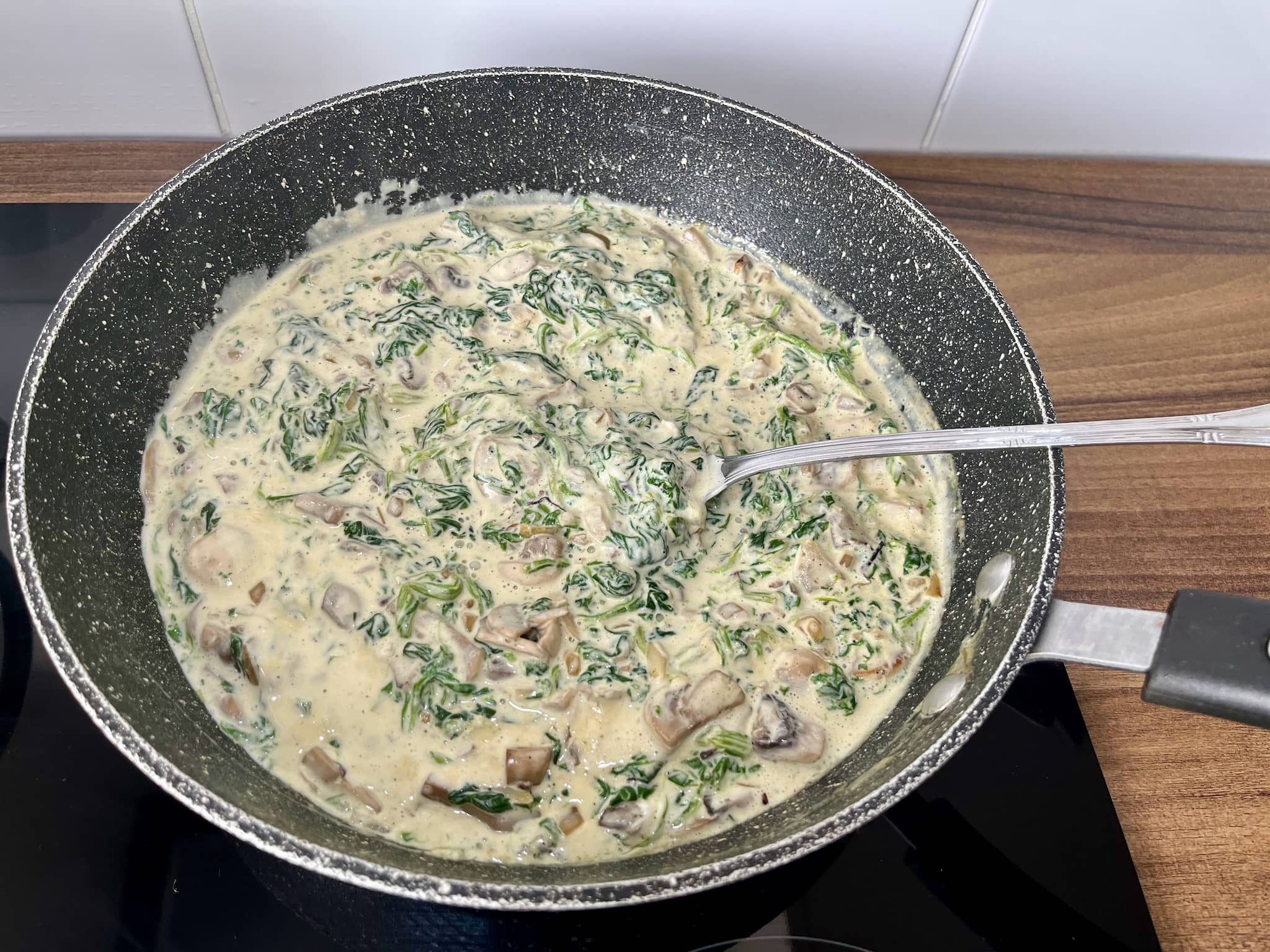 Mushrooms and spinach sizzling in a pan with double cream added