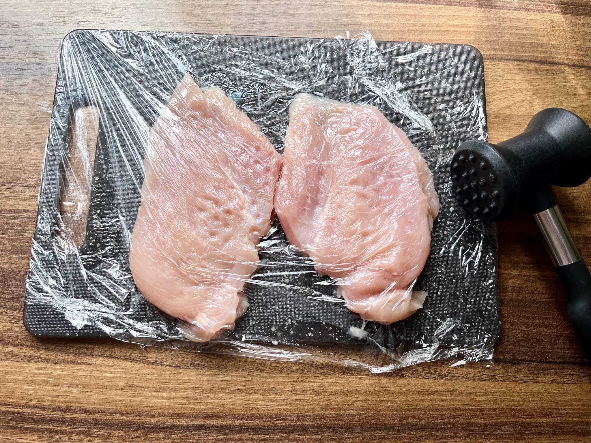 Chicken breasts on a chopping board covered with cling film