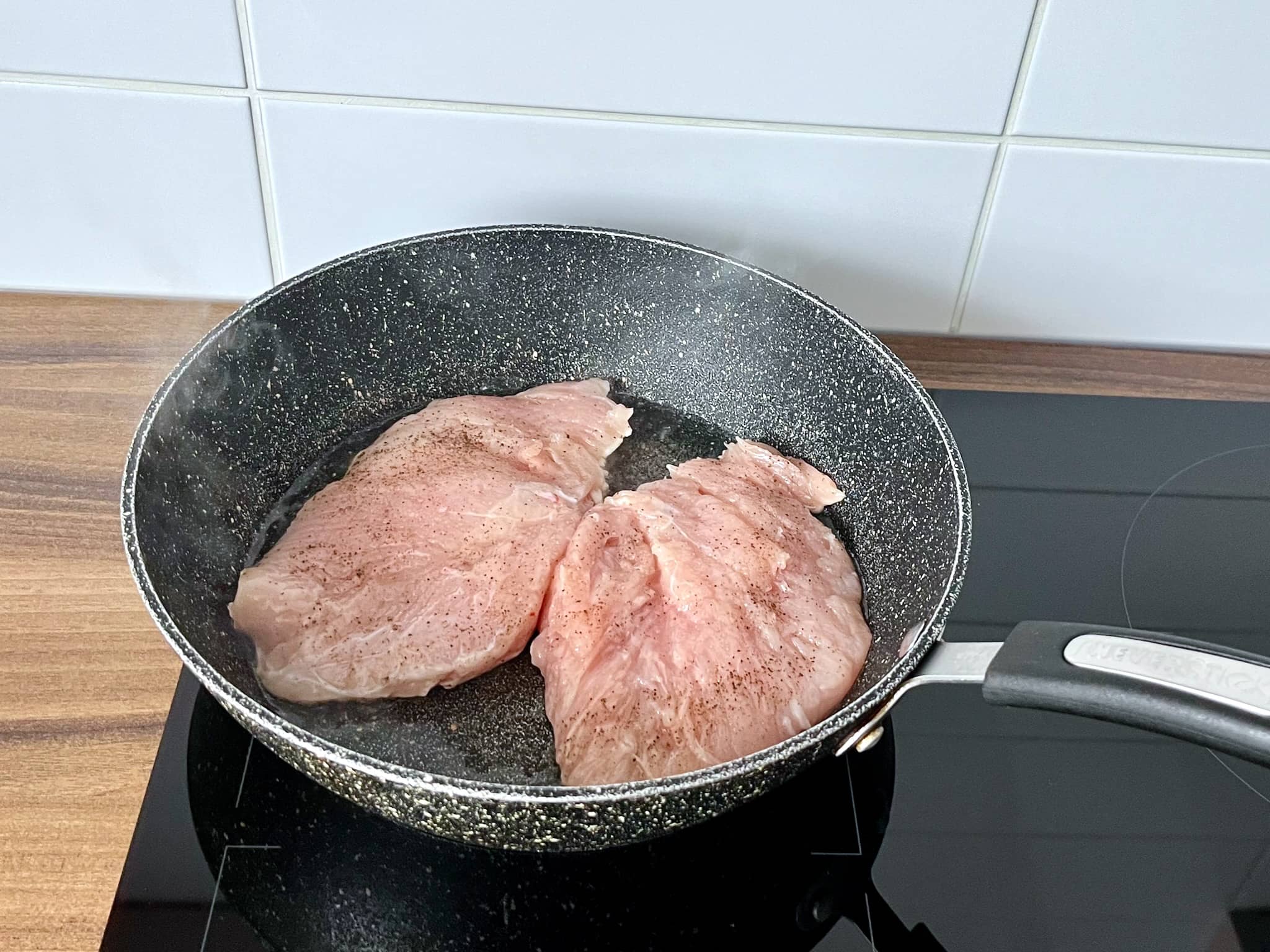 Chicken breasts seasoned with salt and pepper frying in a pan