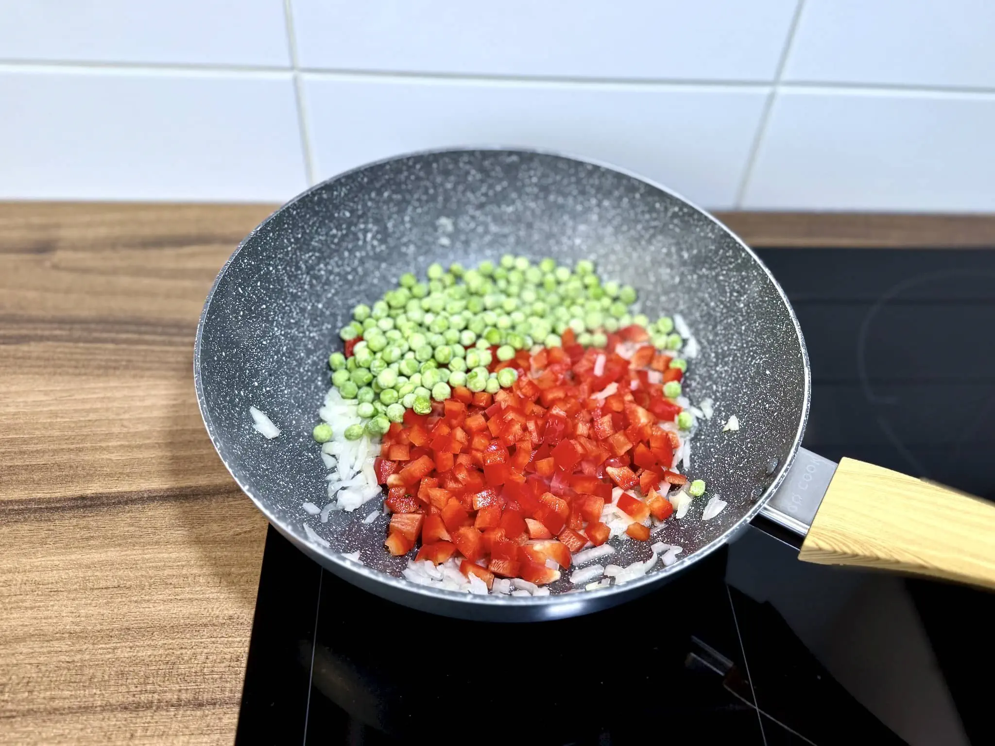 Fried onion in a pan with red bell pepper and frozen peas added on top