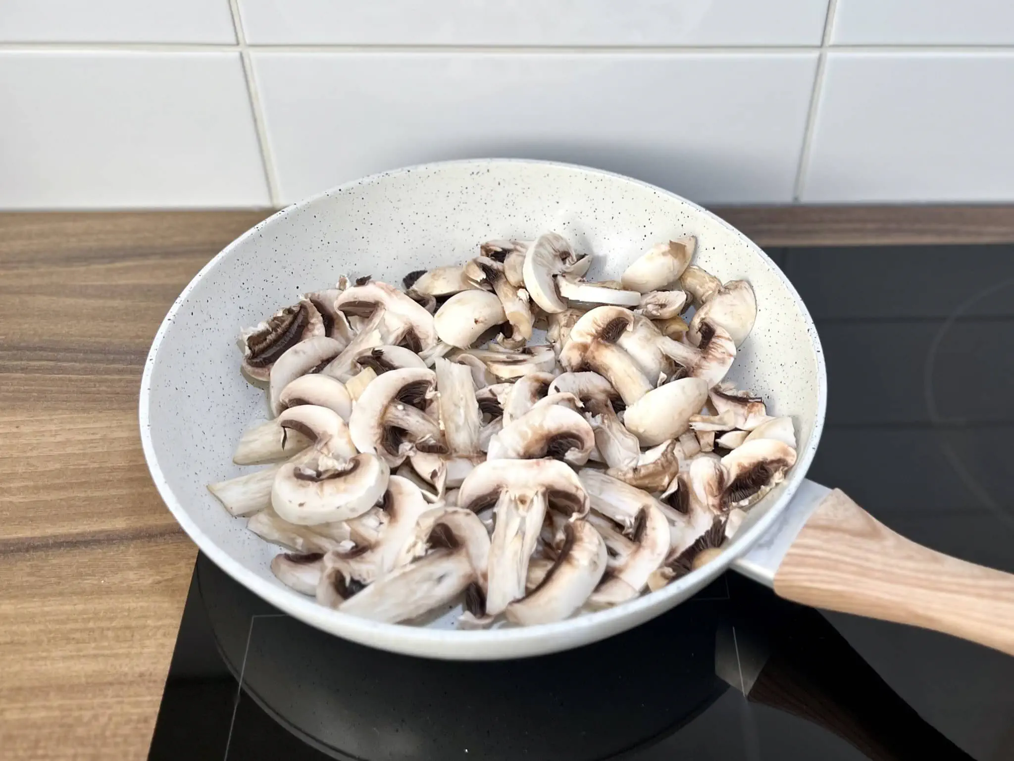 Sliced closed-cup mushrooms cooking in a pan