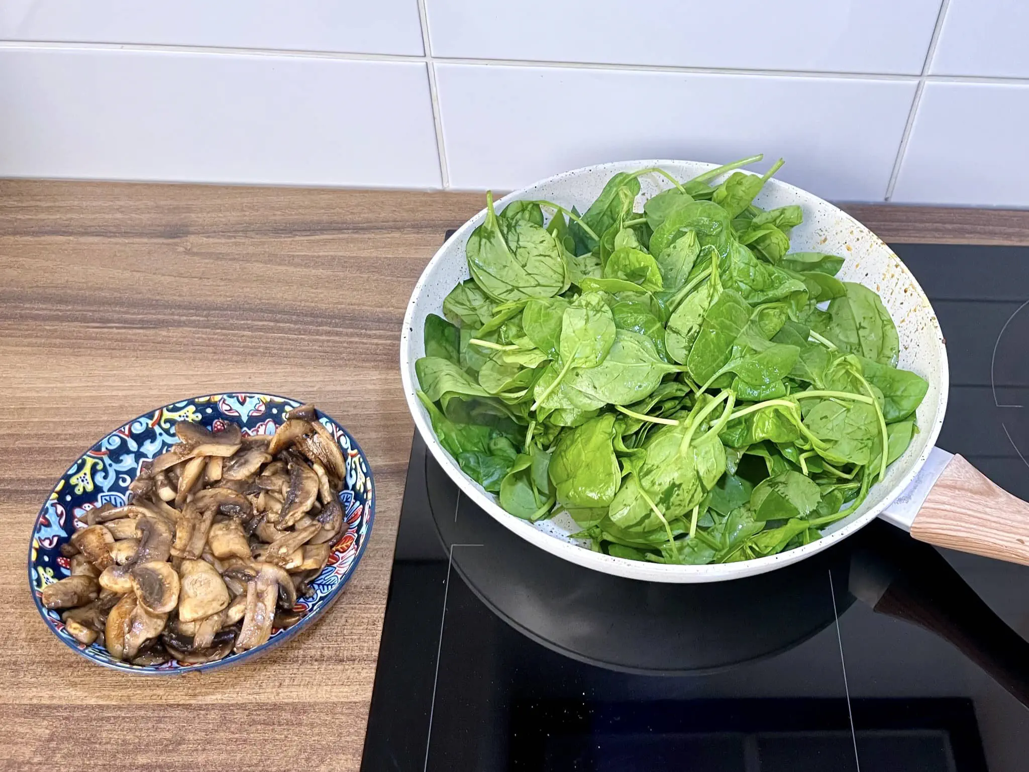 Fried mushrooms set aside in a bowl, with fresh spinach placed in the pan