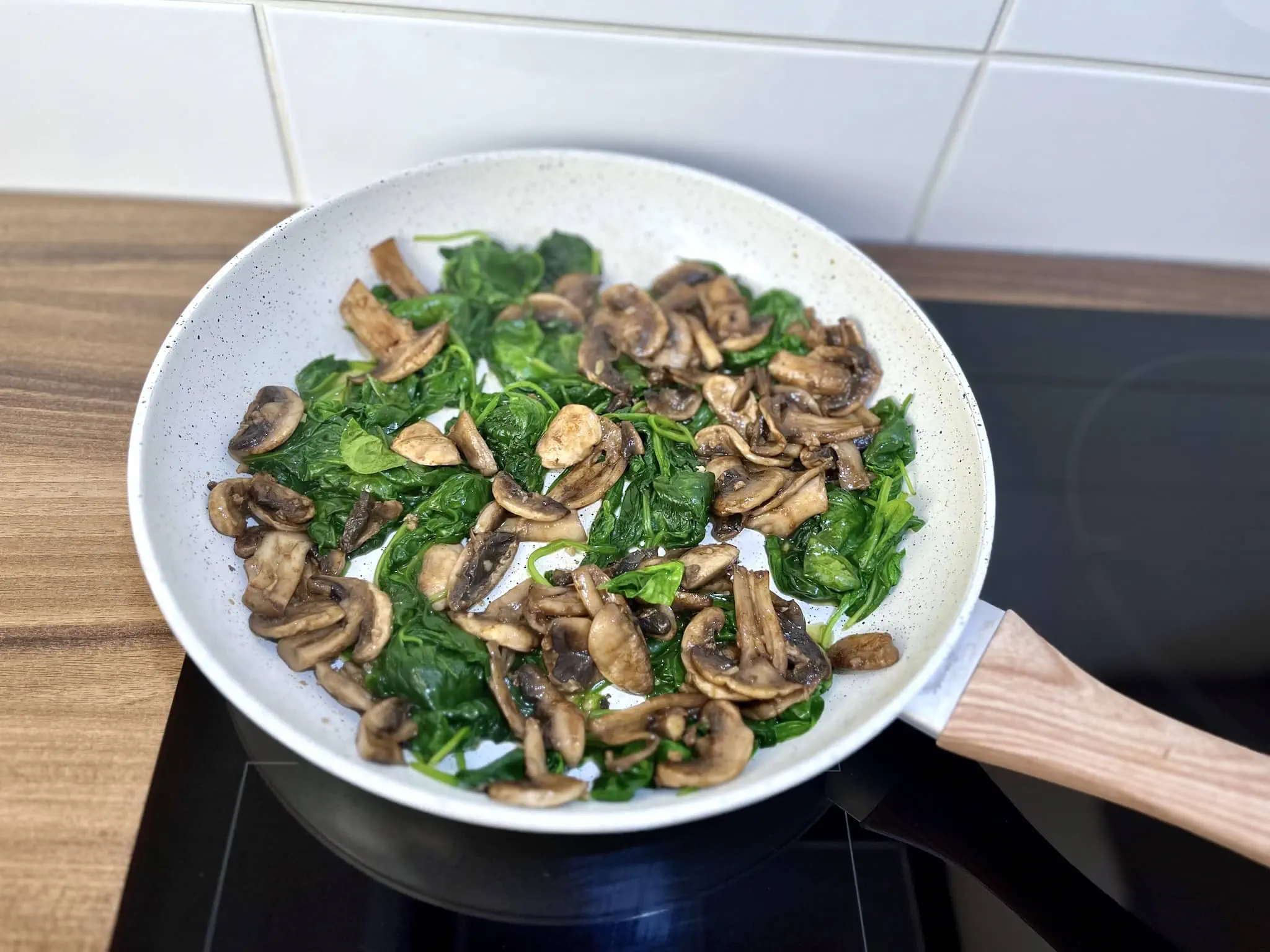Wilted spinach in the pan with mushrooms added back in
