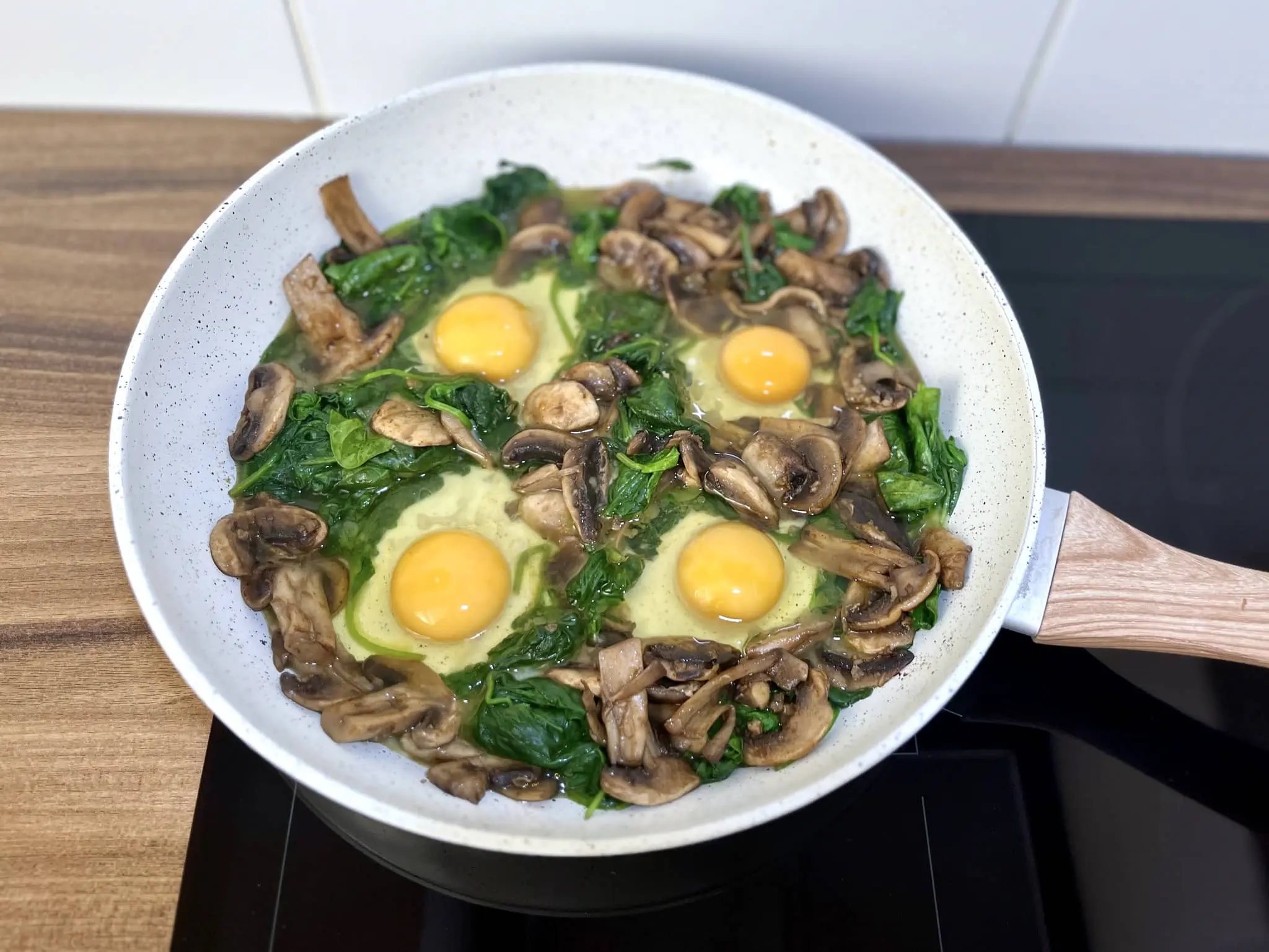 Fresh eggs cracked into the four wells in the pan with spinach and mushrooms